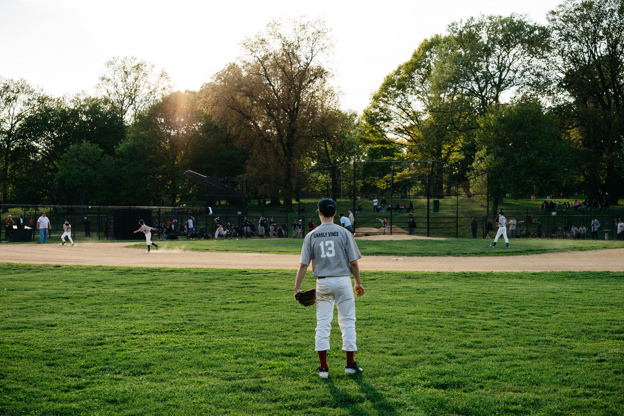 Baseball player in a park, facing away from the camera.