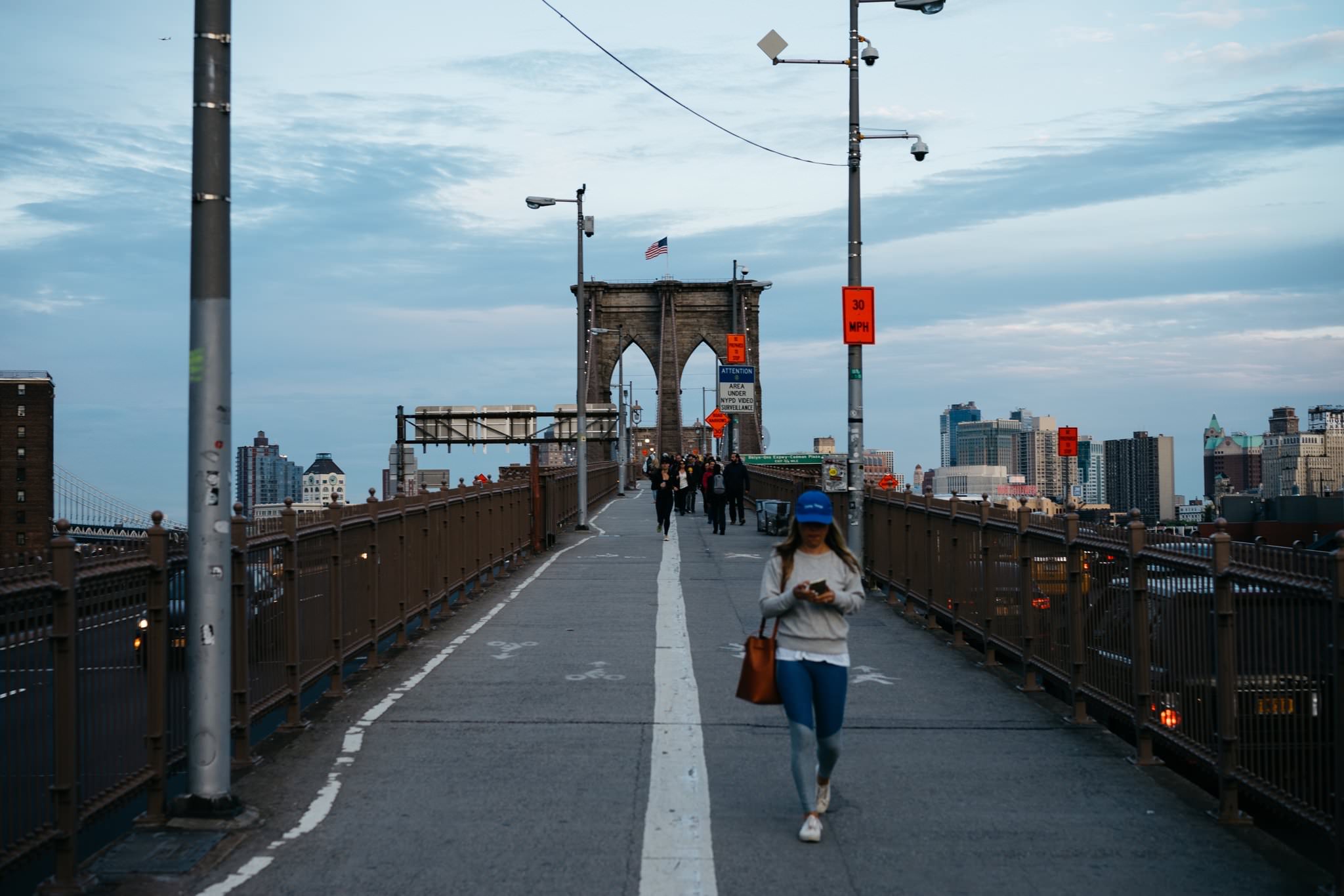 Woman on Brooklyn Bridge walkway, NYC skyline in background.