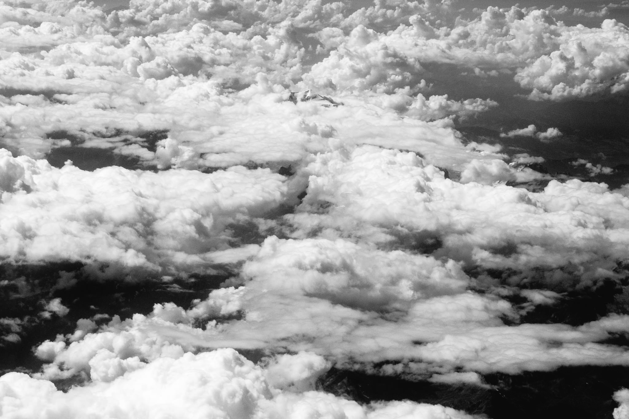 Black and white aerial view of fluffy clouds covering mountains.