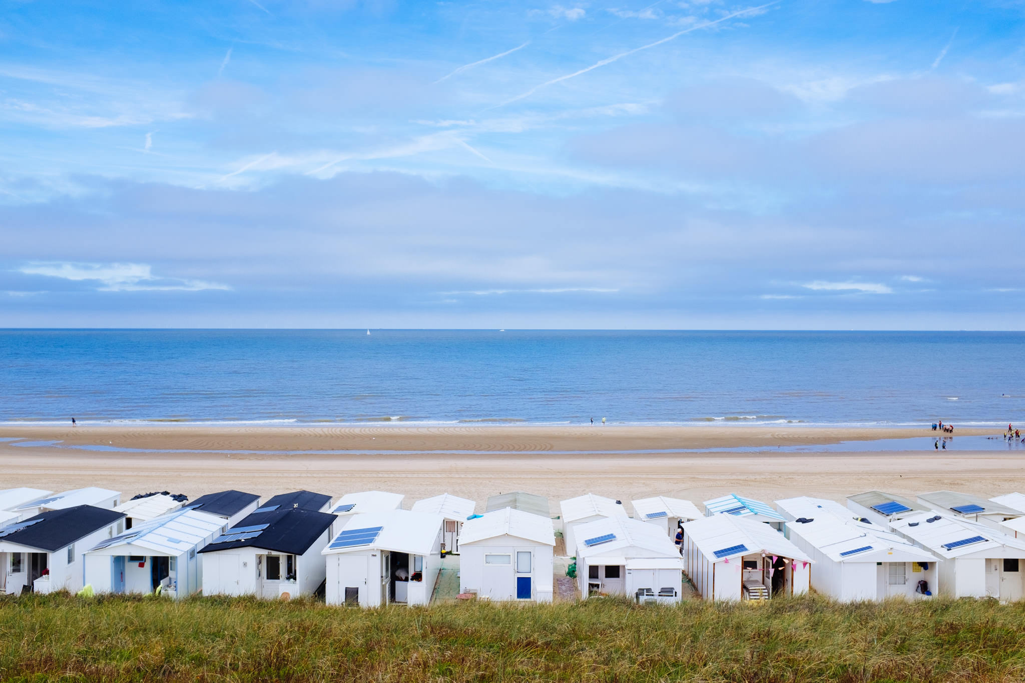 Row of white beach cottages with solar panels, overlooking a sandy beach and ocean.
