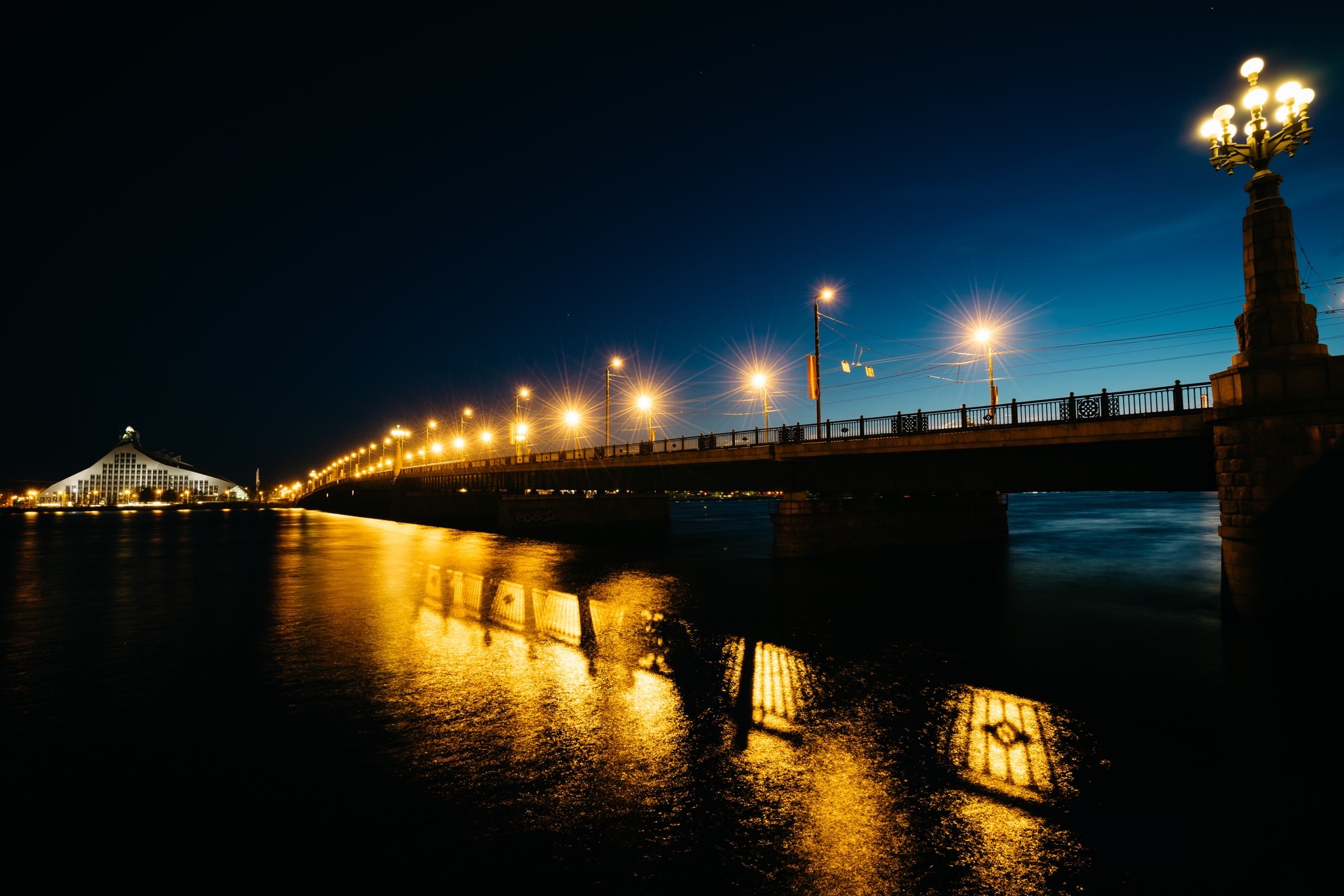 Night view of a lit bridge over a dark river reflecting the lights.
