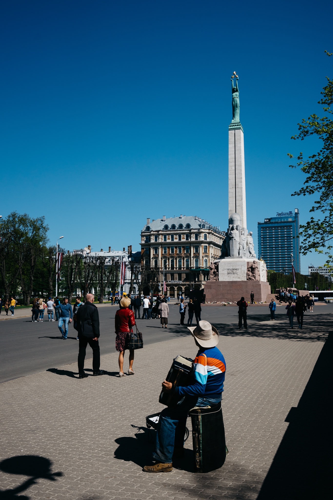 Freedom Monument in Riga, Latvia, with a street musician playing an accordion in the foreground.
