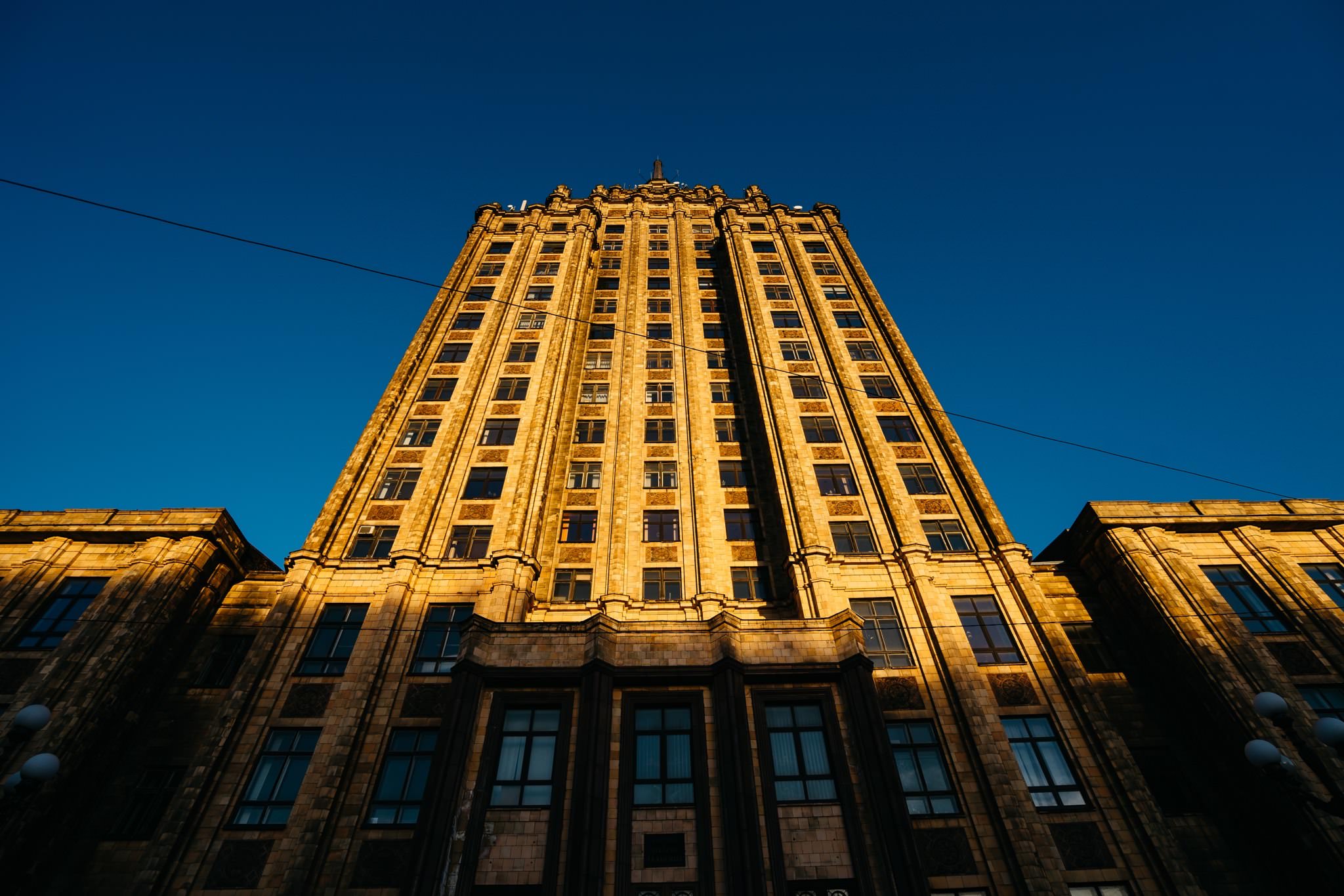 Low-angle view of the Latvian Academy of Sciences building in Riga, illuminated by golden sunlight against a clear blue sky.