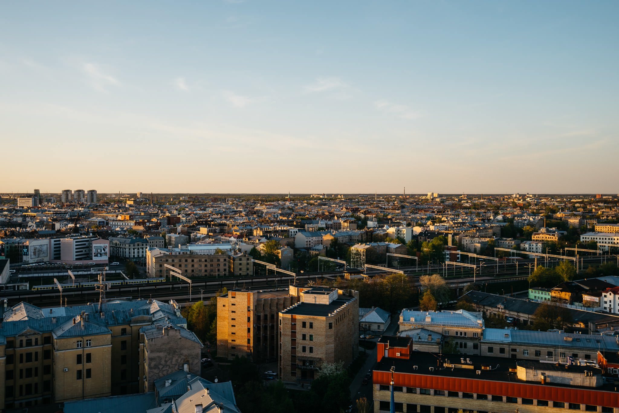 Panoramic view of Riga, Latvia at sunset, showing a cityscape with railway tracks.