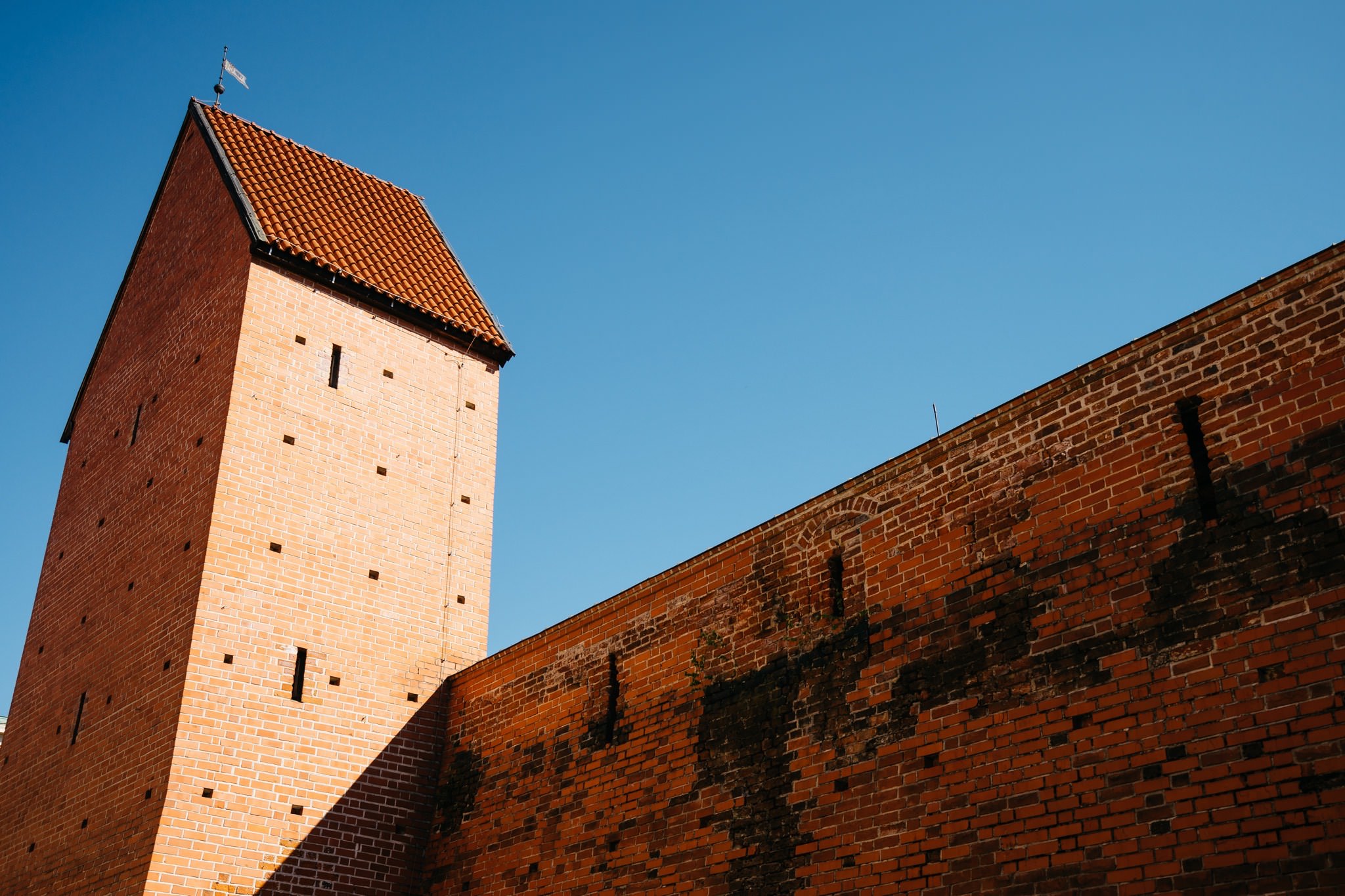 Brick tower and wall against a clear blue sky.