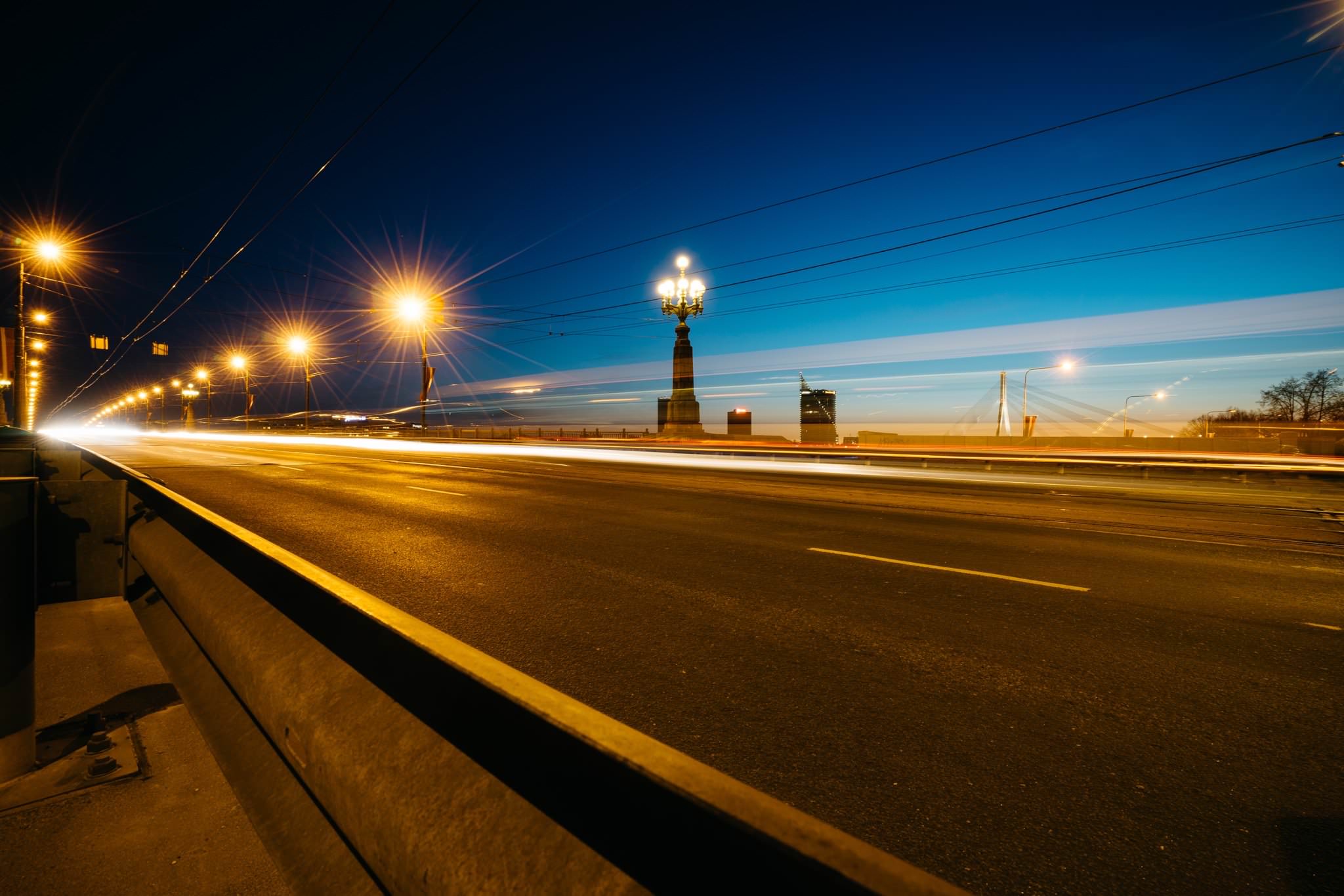 Nighttime long exposure of a Riga, Latvia bridge with light trails from moving vehicles.