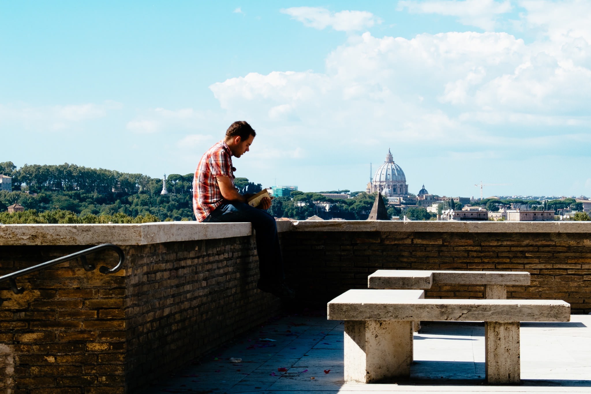 Man reading book on a brick wall overlooking Rome, Italy.