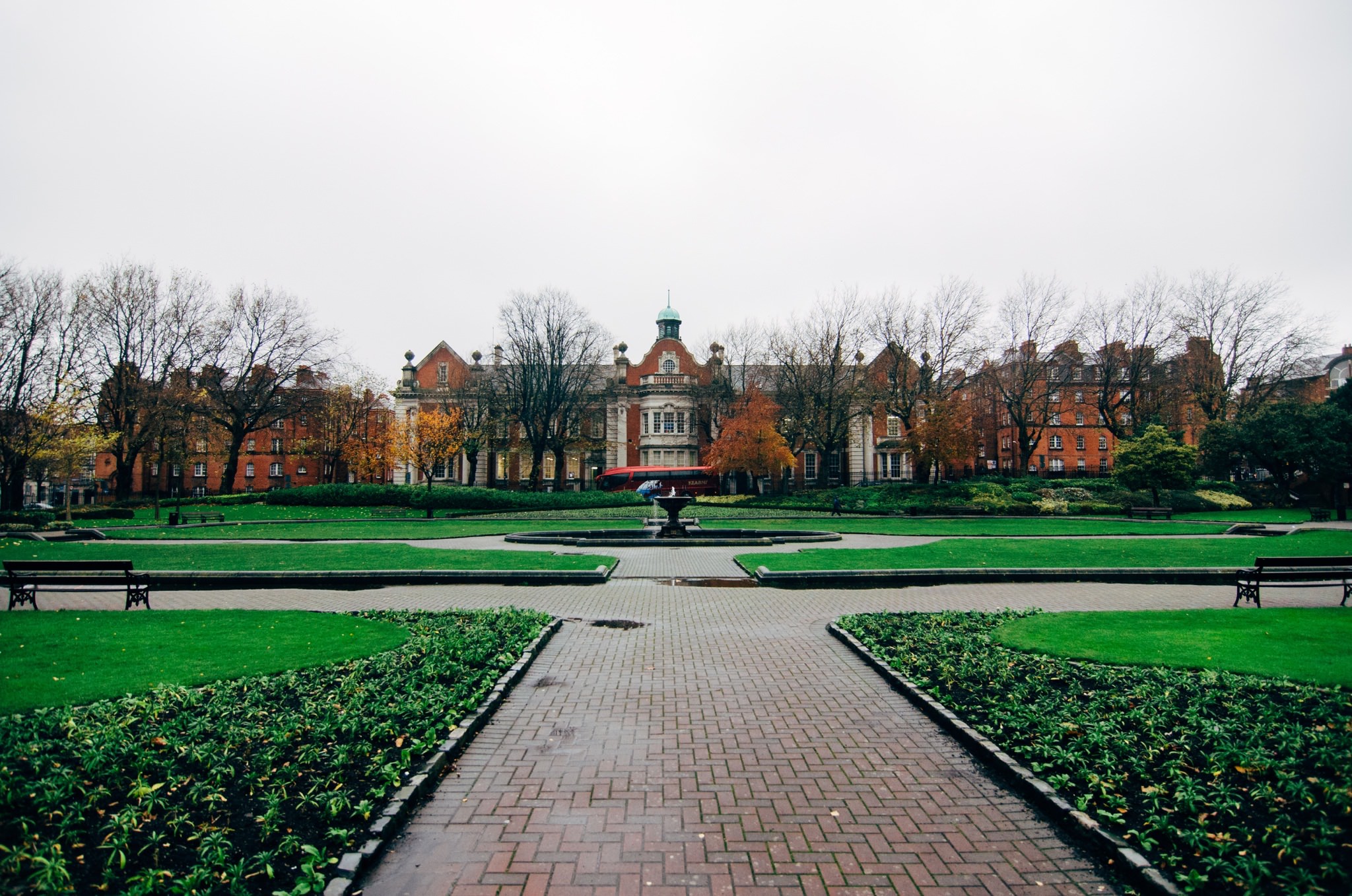 Saint Patrick's Park with a large brick building in the background and a fountain in the foreground.