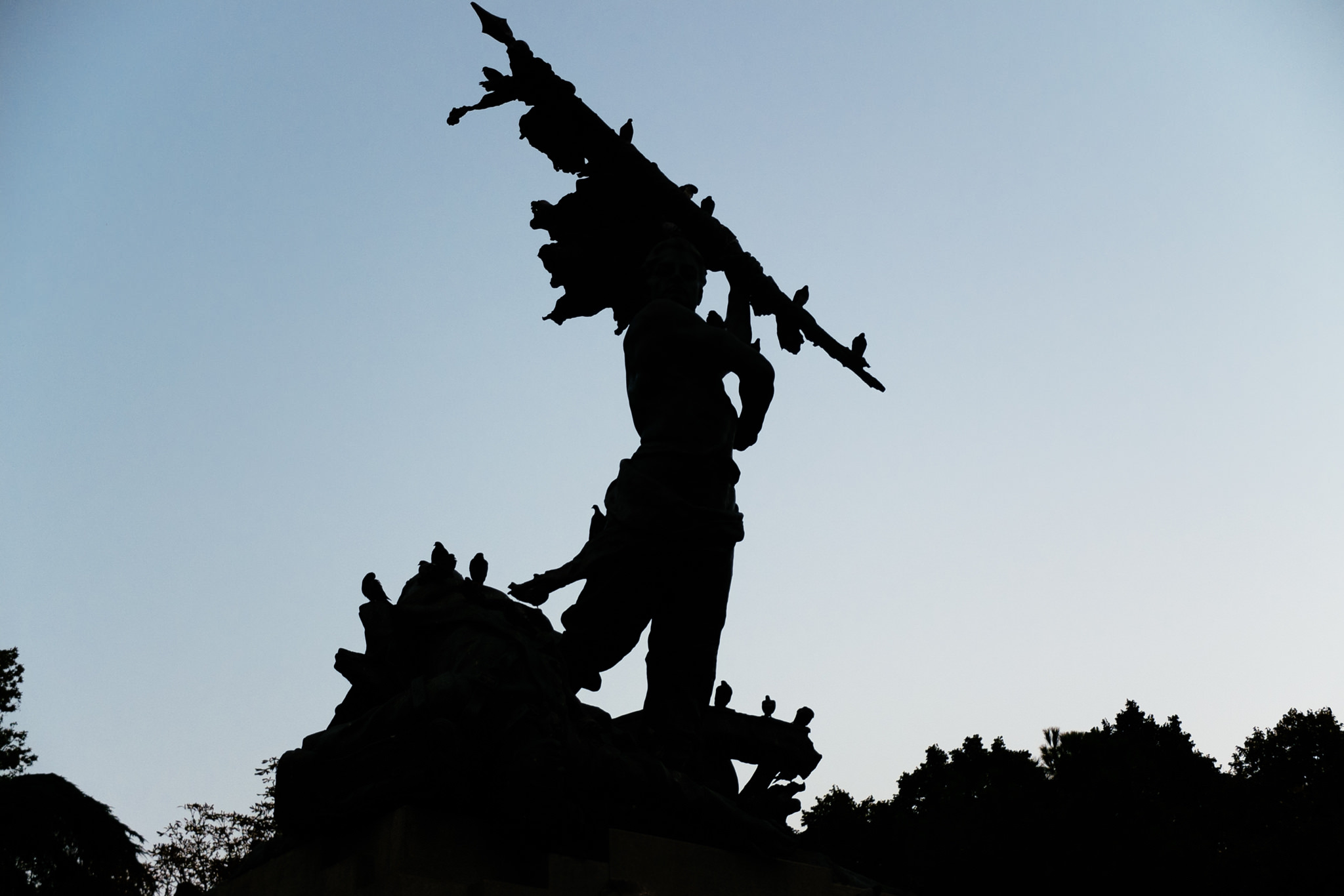 Silhouette of a statue carrying a large branch, with birds perched on the statue and branch.
