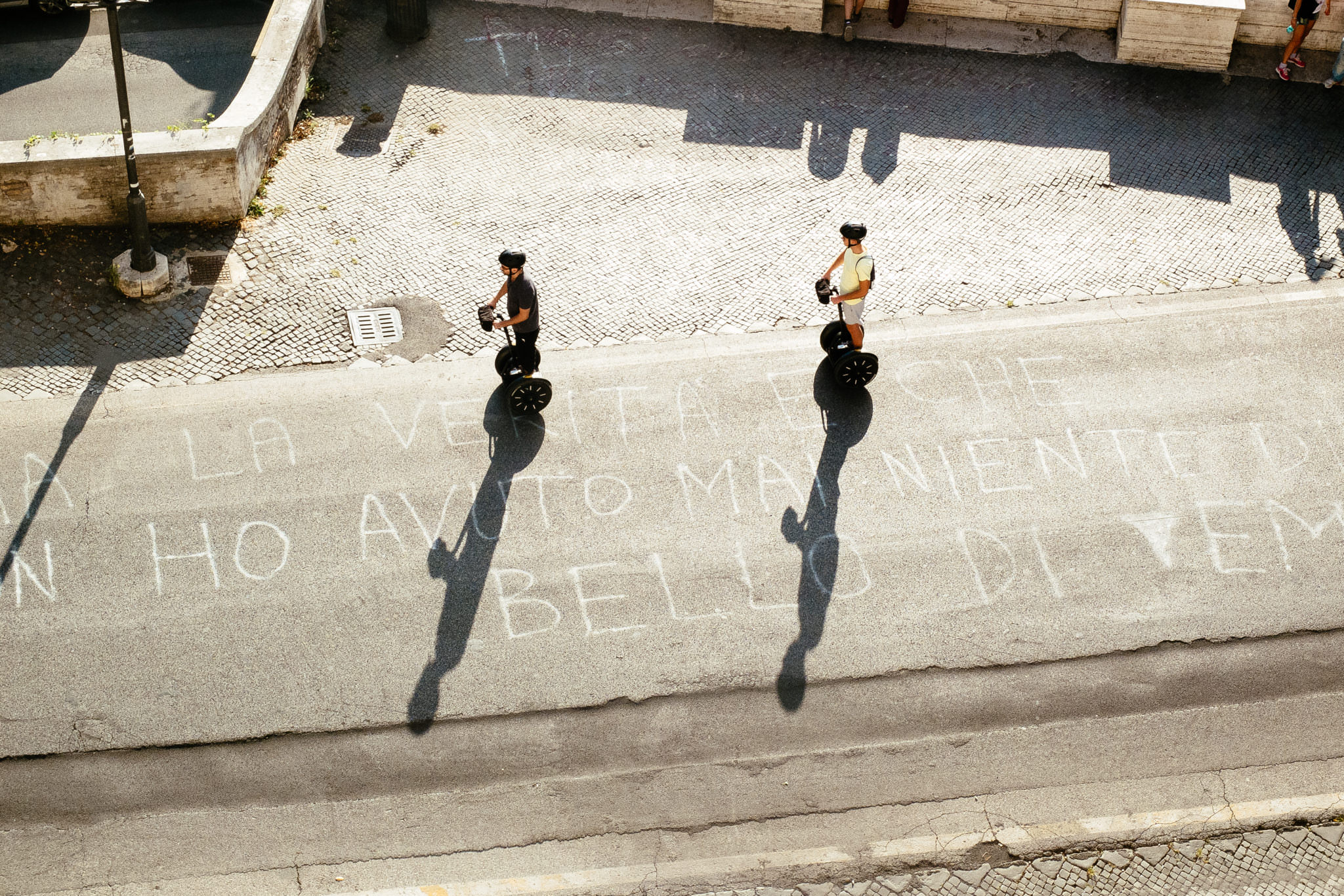 Two people riding Segways on a street with chalk writing on the pavement.