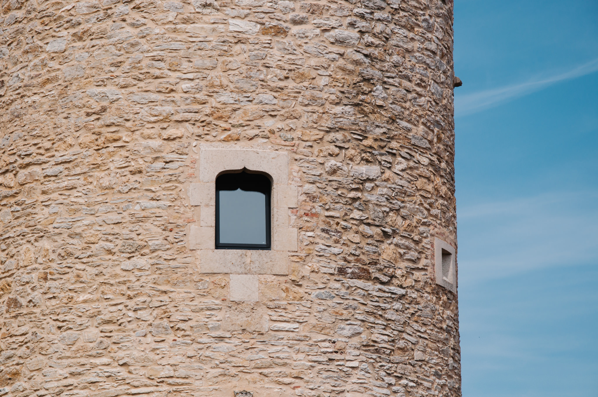 Stone tower with small arched window against a blue sky.