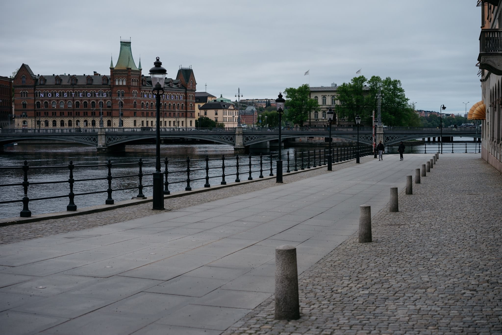 Empty waterfront walkway in Stockholm, Sweden, with a bridge and buildings in the background.