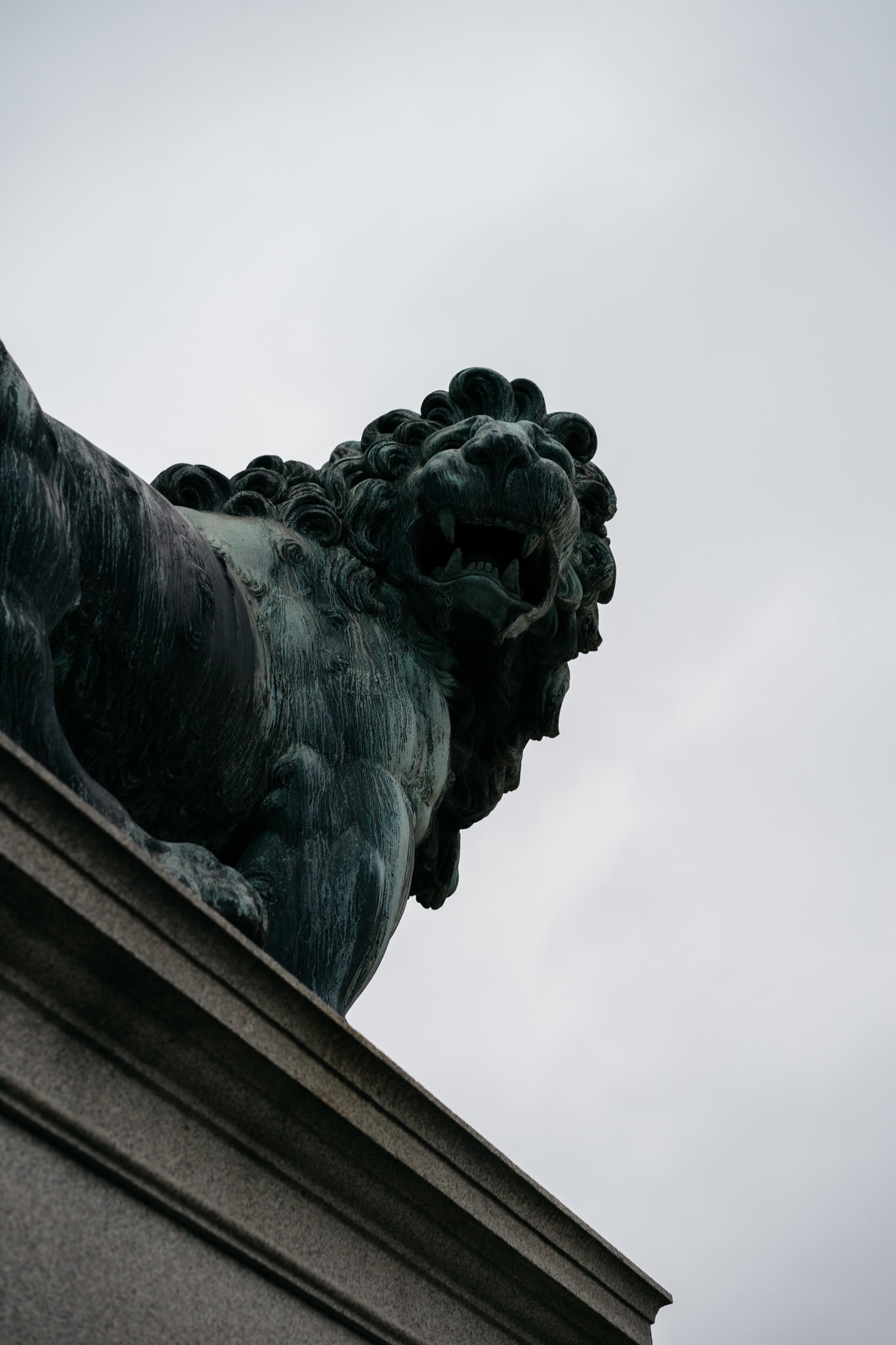 Low-angle view of a dark bronze lion statue atop a stone wall.
