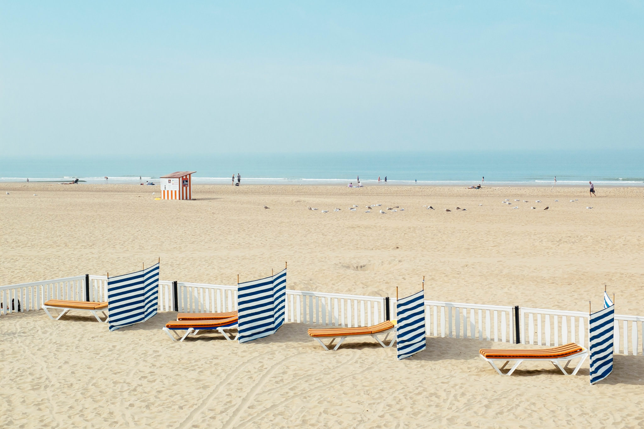 Beach with striped windbreaks and orange lounge chairs.