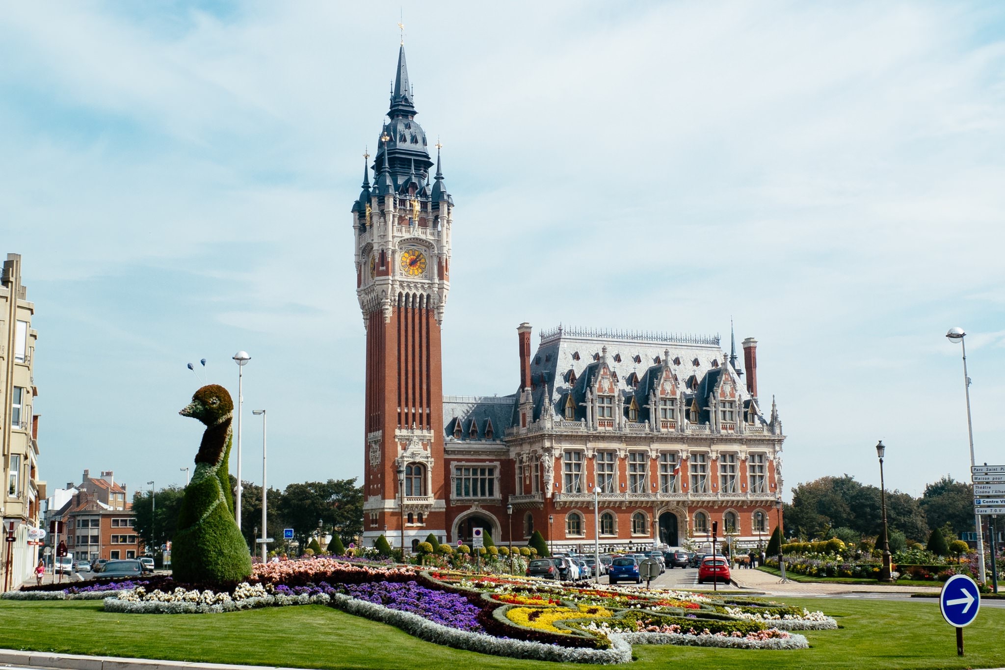 Calais town hall with a tall clock tower and flower garden.