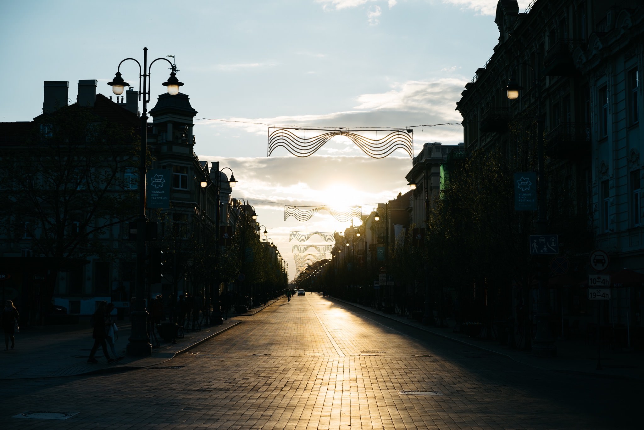Sunset view of a Vilnius, Lithuania street with decorative lights strung overhead.