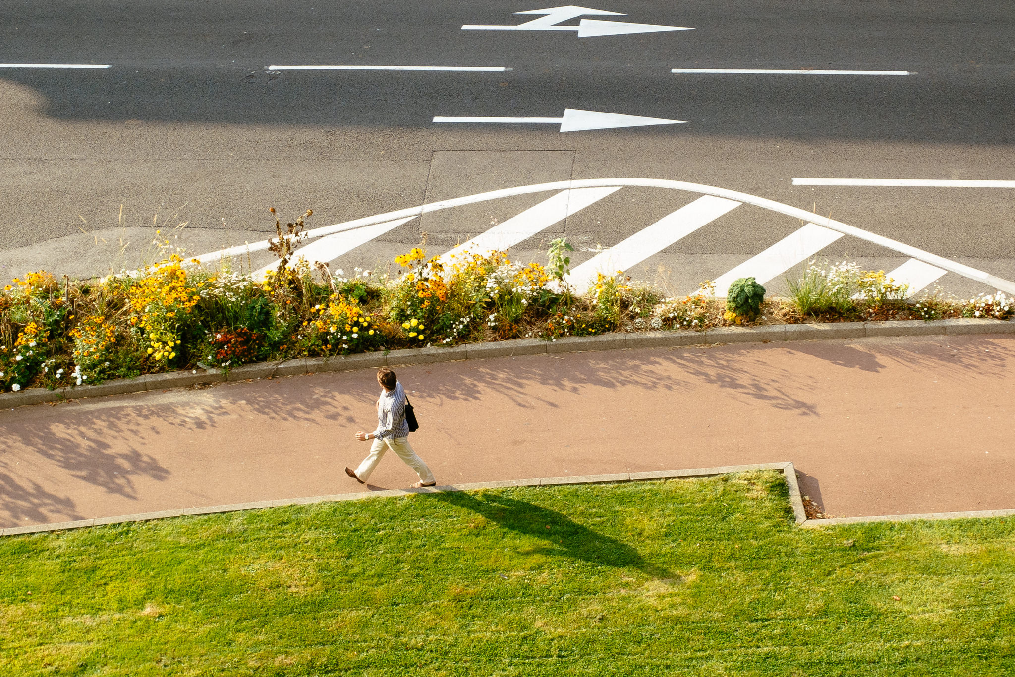 Man walking on pedestrian path next to roadway with painted arrows.