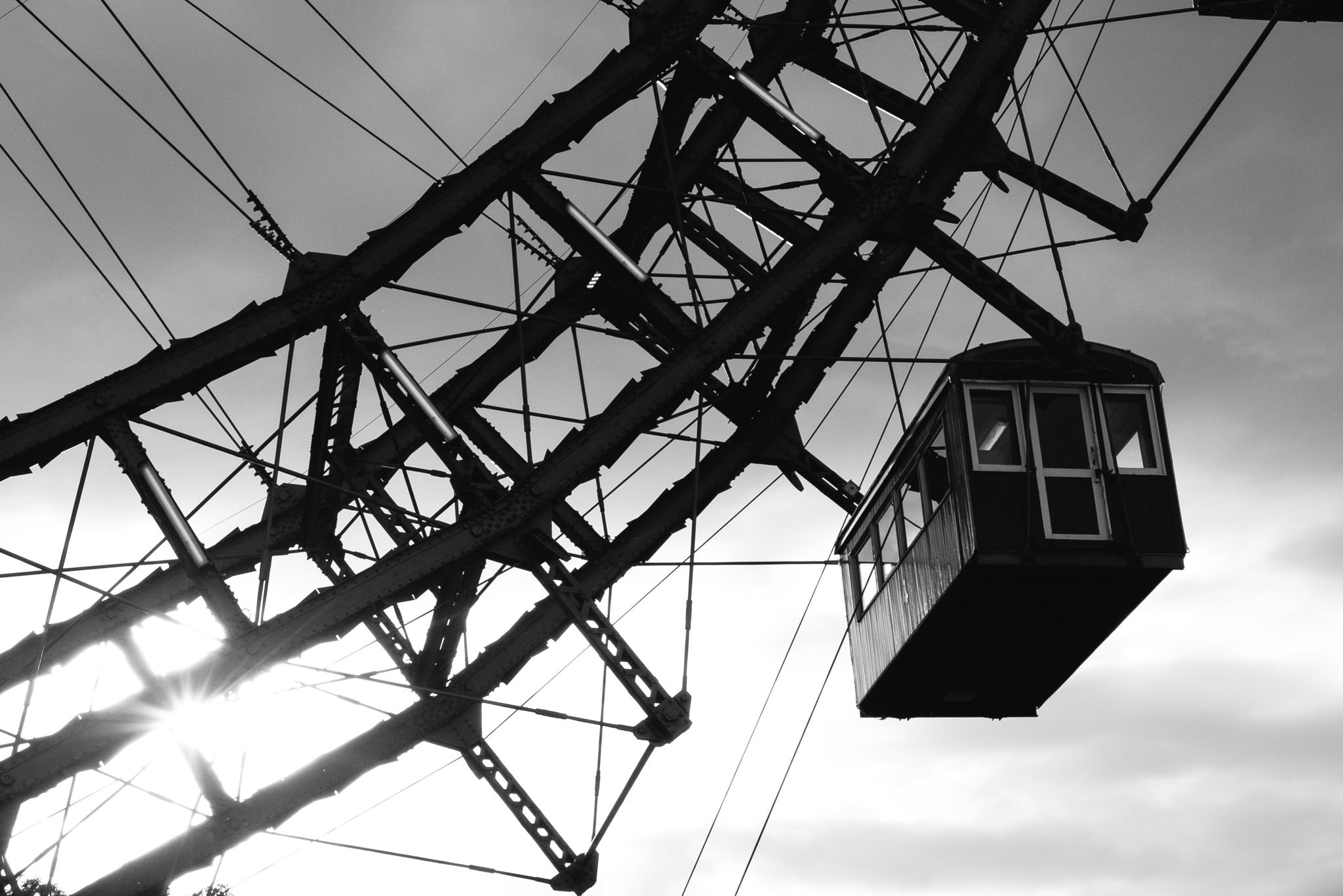 Black and white photo of a Ferris wheel gondola and structural support against a cloudy sky.