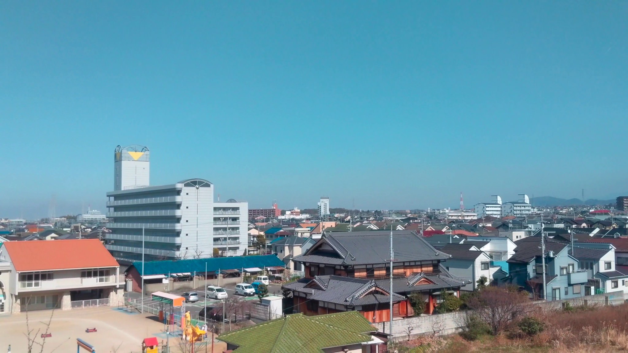 Aerial view of a residential area in Osaka, Japan, near Kansai International Airport, featuring a mix of modern and traditional houses under a clear blue sky.