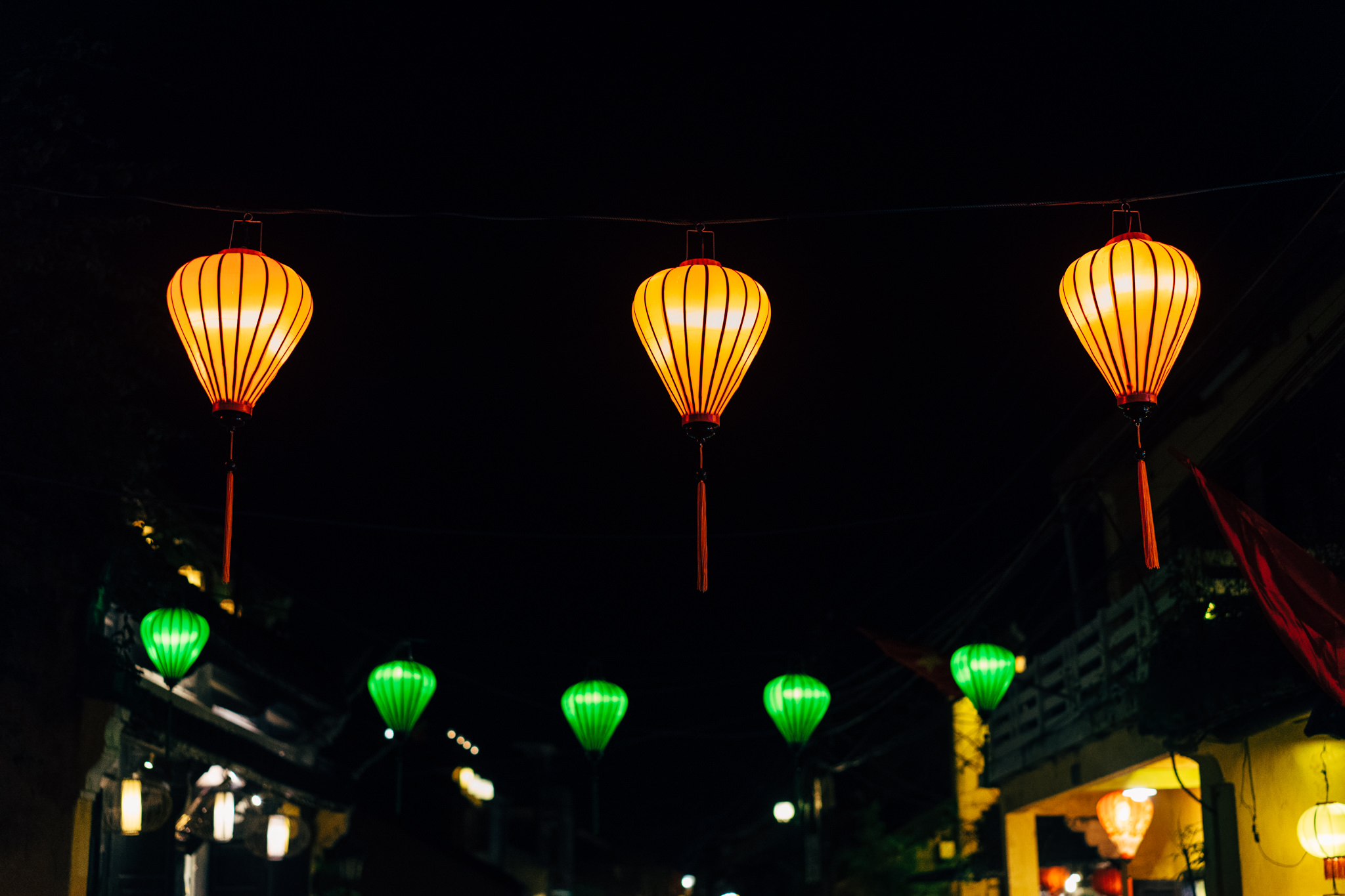 Three illuminated orange lanterns hanging from a wire at night.