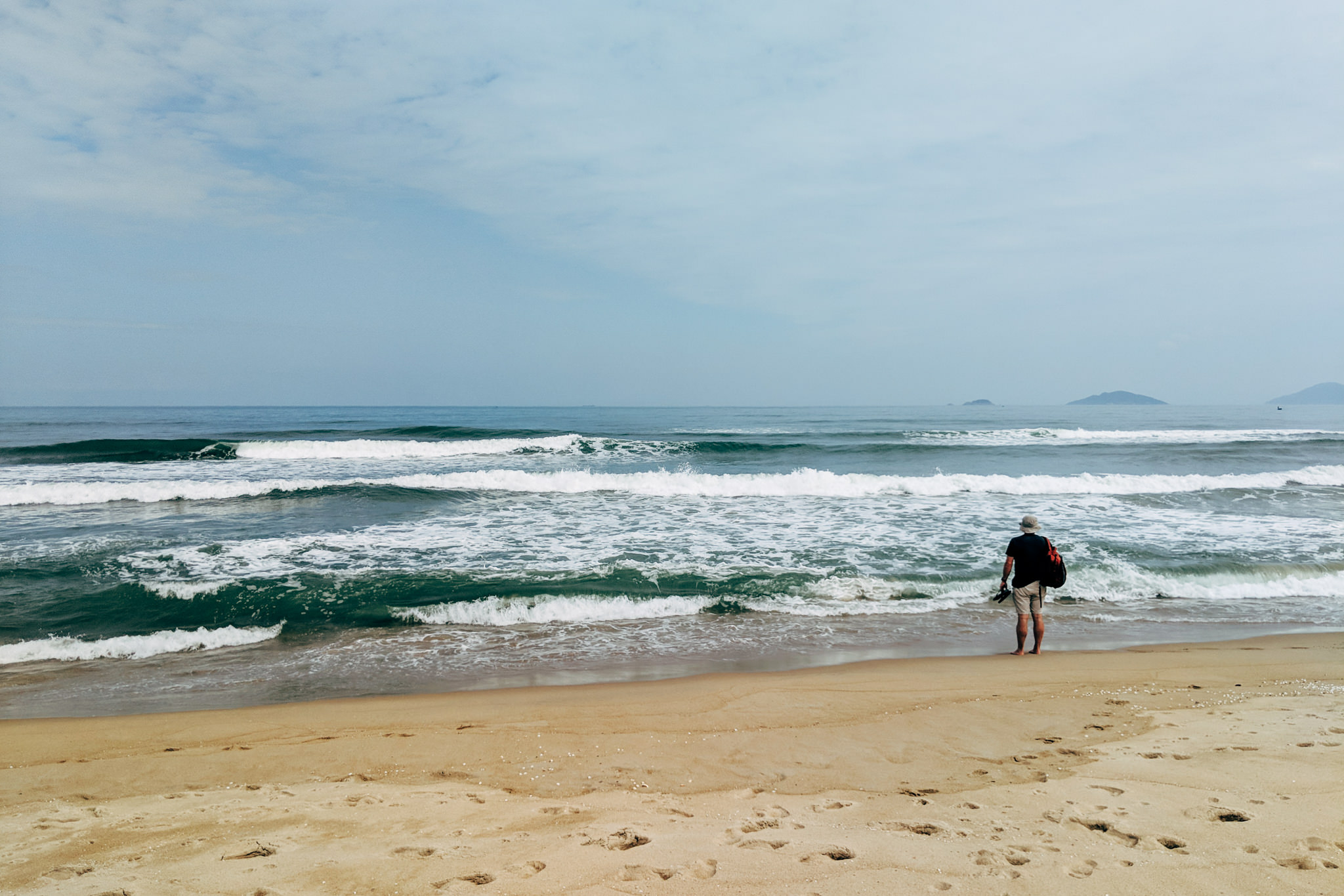Man standing on An Bang Beach in Vietnam, facing the ocean.