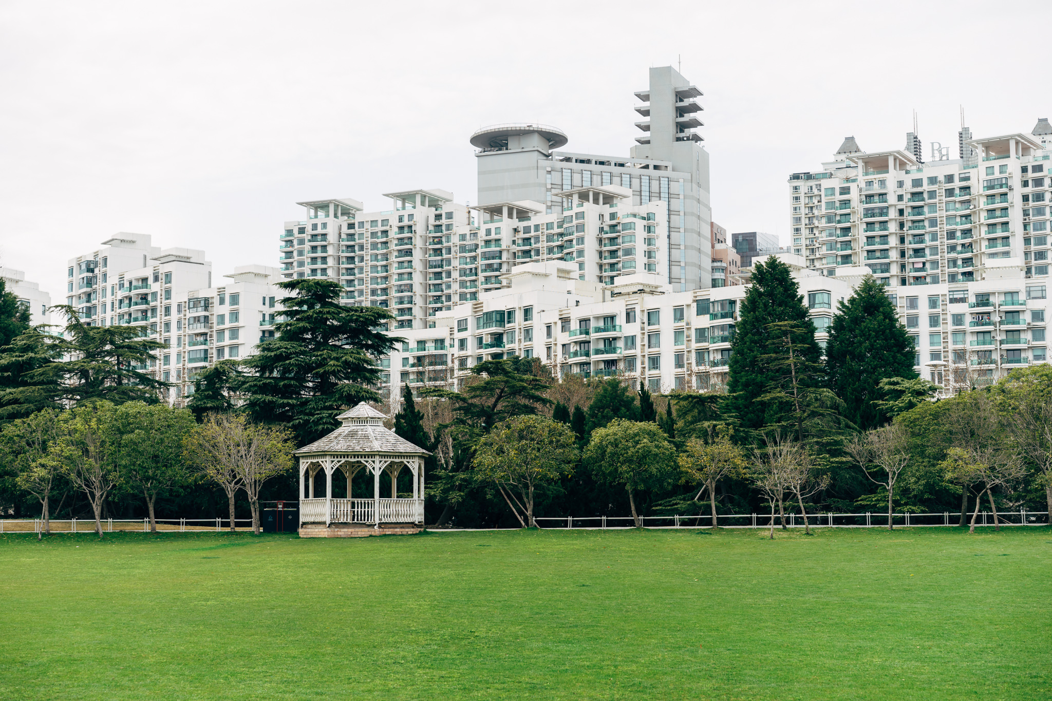 White gazebo in a grassy park with tall residential buildings in the background.