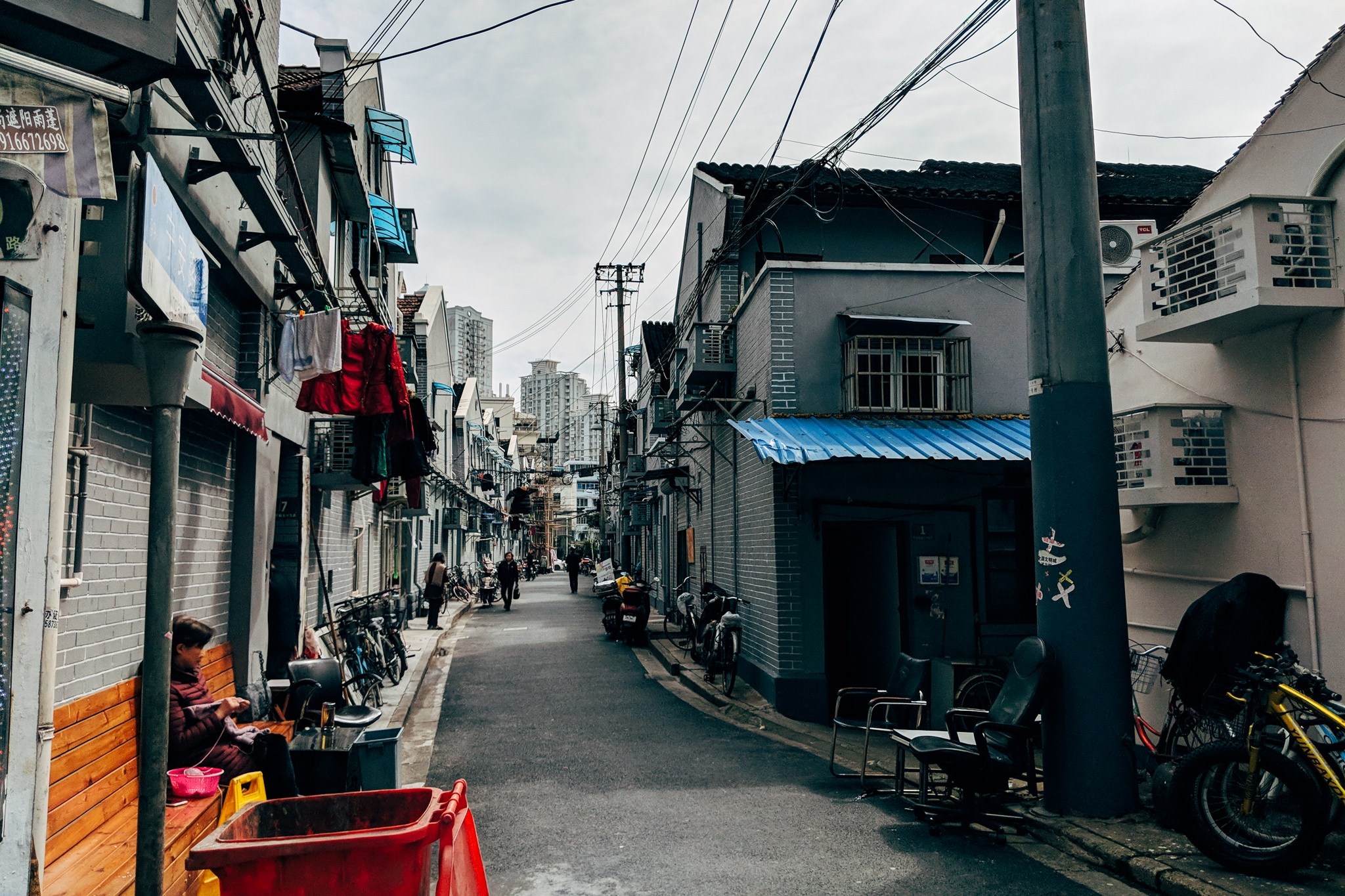 Narrow Shanghai alleyway with residential buildings, laundry hanging from lines, and people walking.