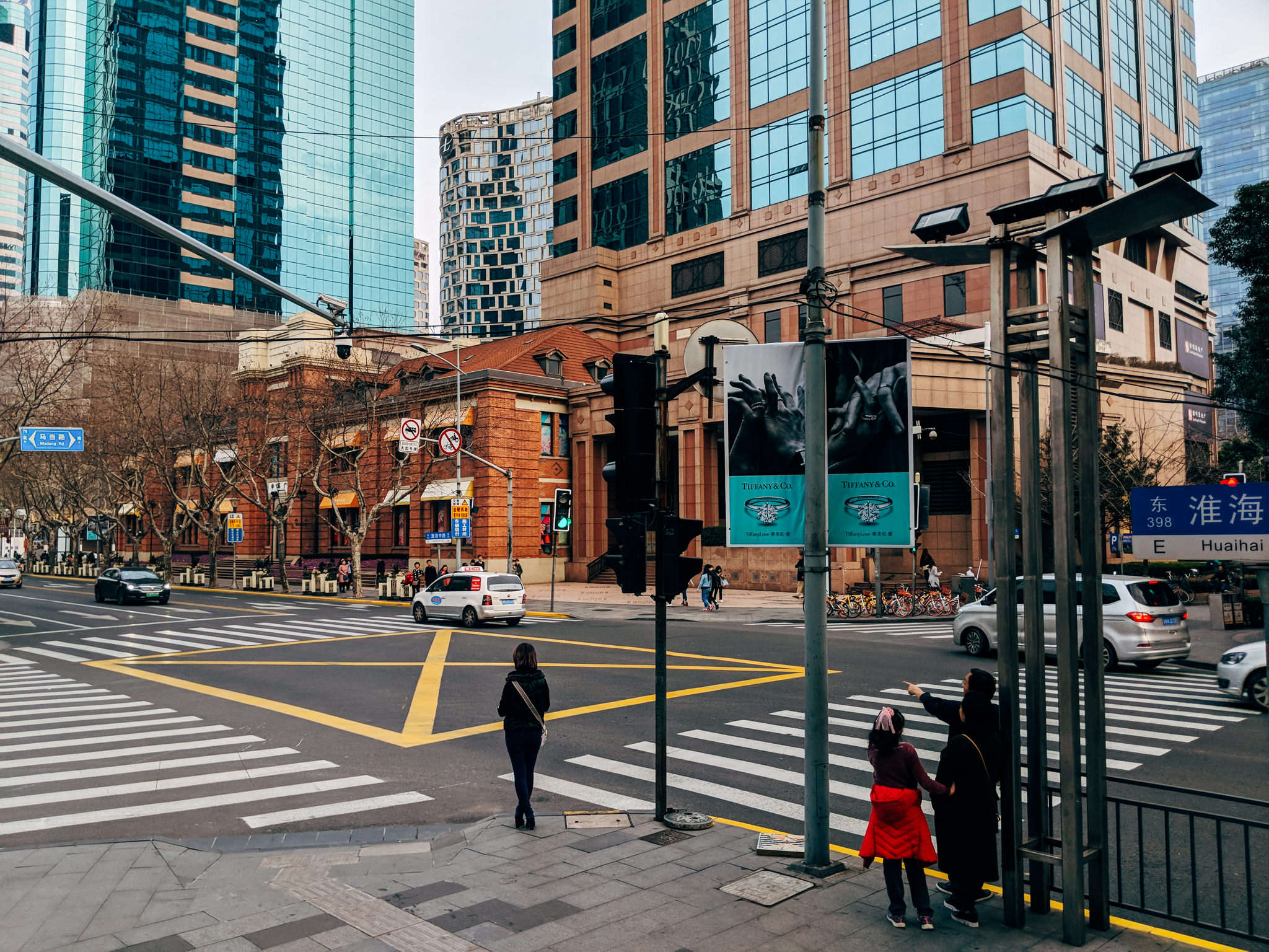 Shanghai street scene with pedestrians crossing at a crosswalk, modern and older buildings in the background.