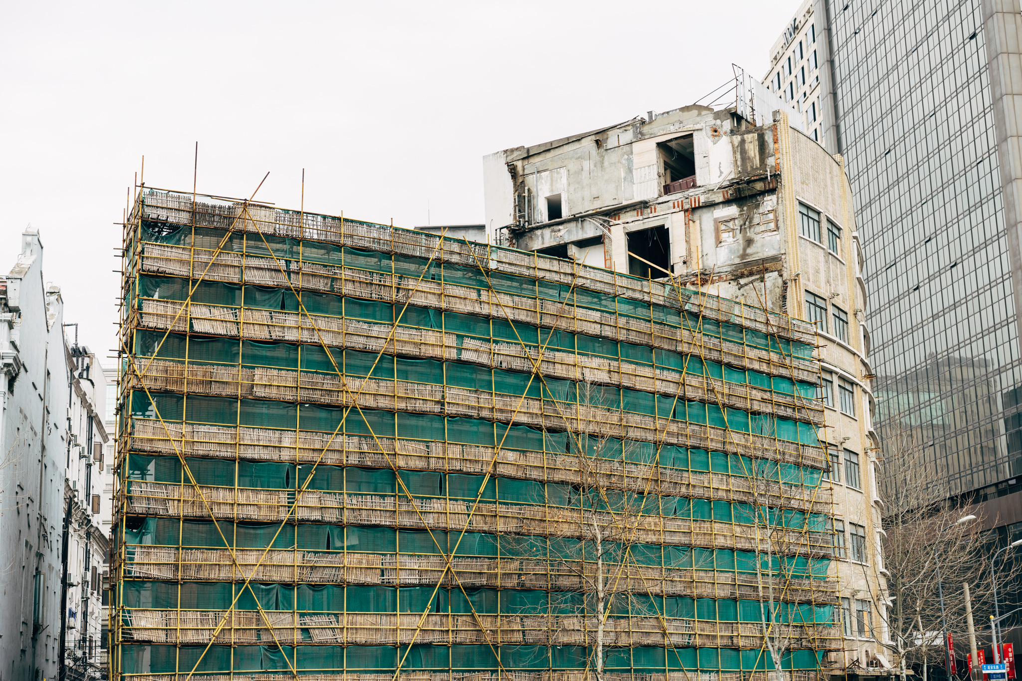 Shanghai building under construction, covered in bamboo scaffolding and green netting.