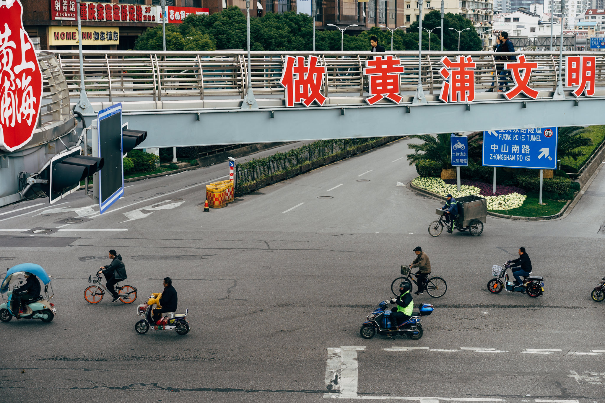 Shanghai street scene with pedestrians on an overpass and people on bicycles and scooters below.