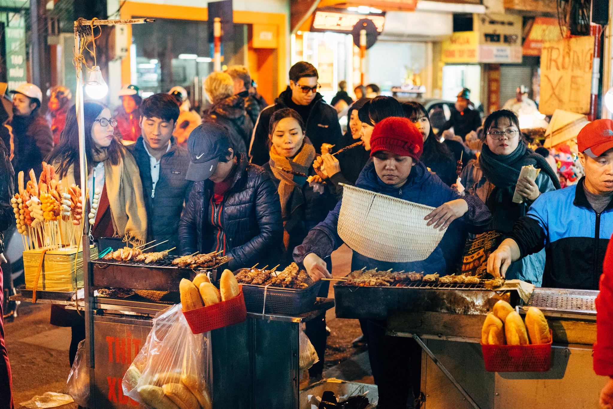 Hanoi street food vendor grilling meat skewers and selling bread at night.
