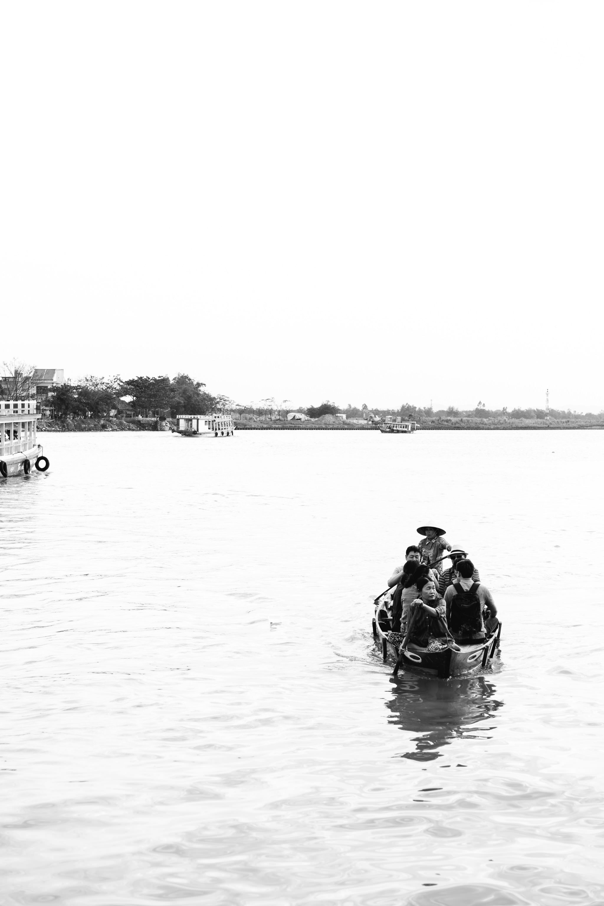 Black and white photo of a small boat carrying several people on a river.