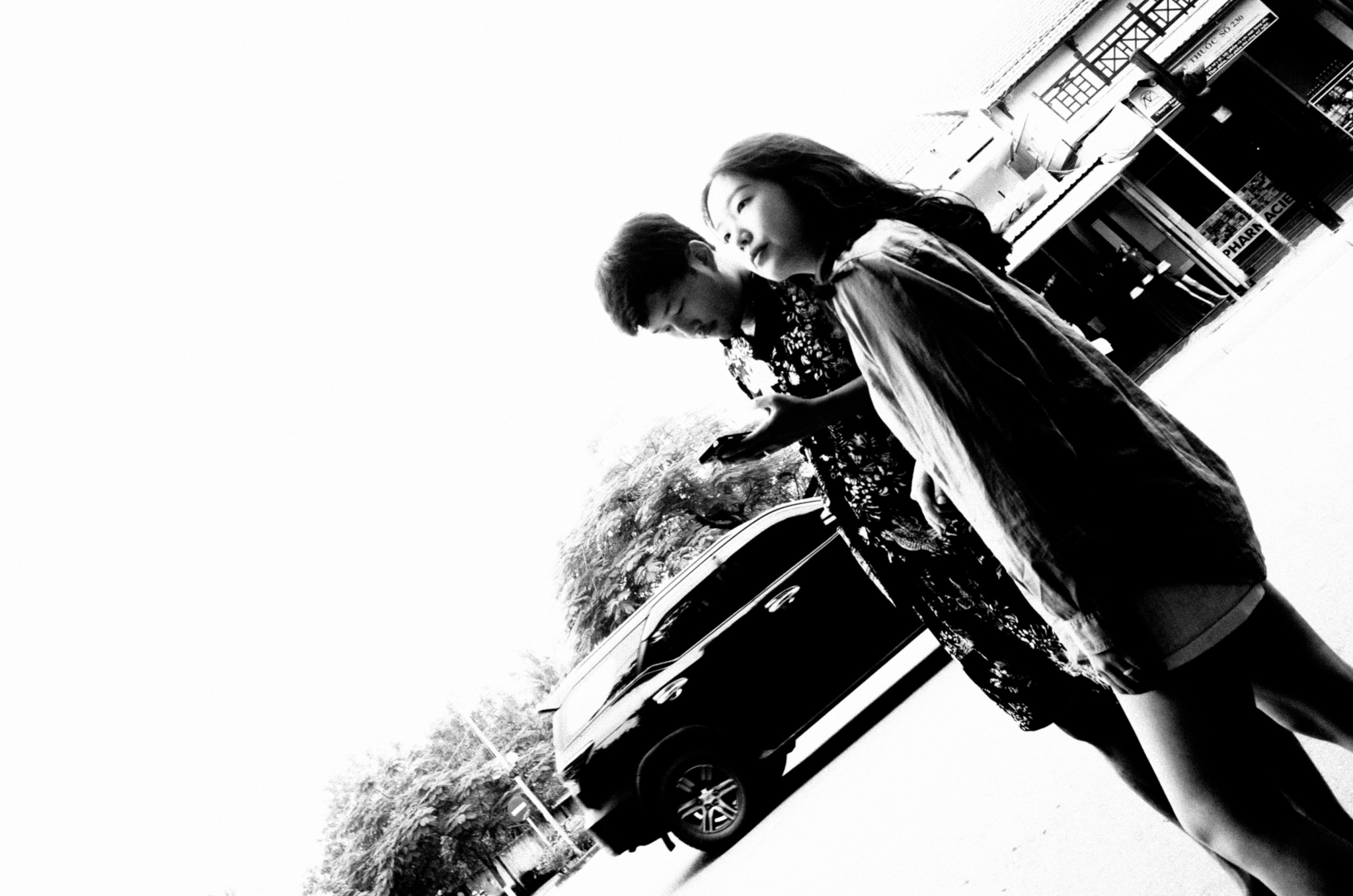 Black and white photo of two young women walking down a street in Hoi An, Vietnam, looking at a phone.