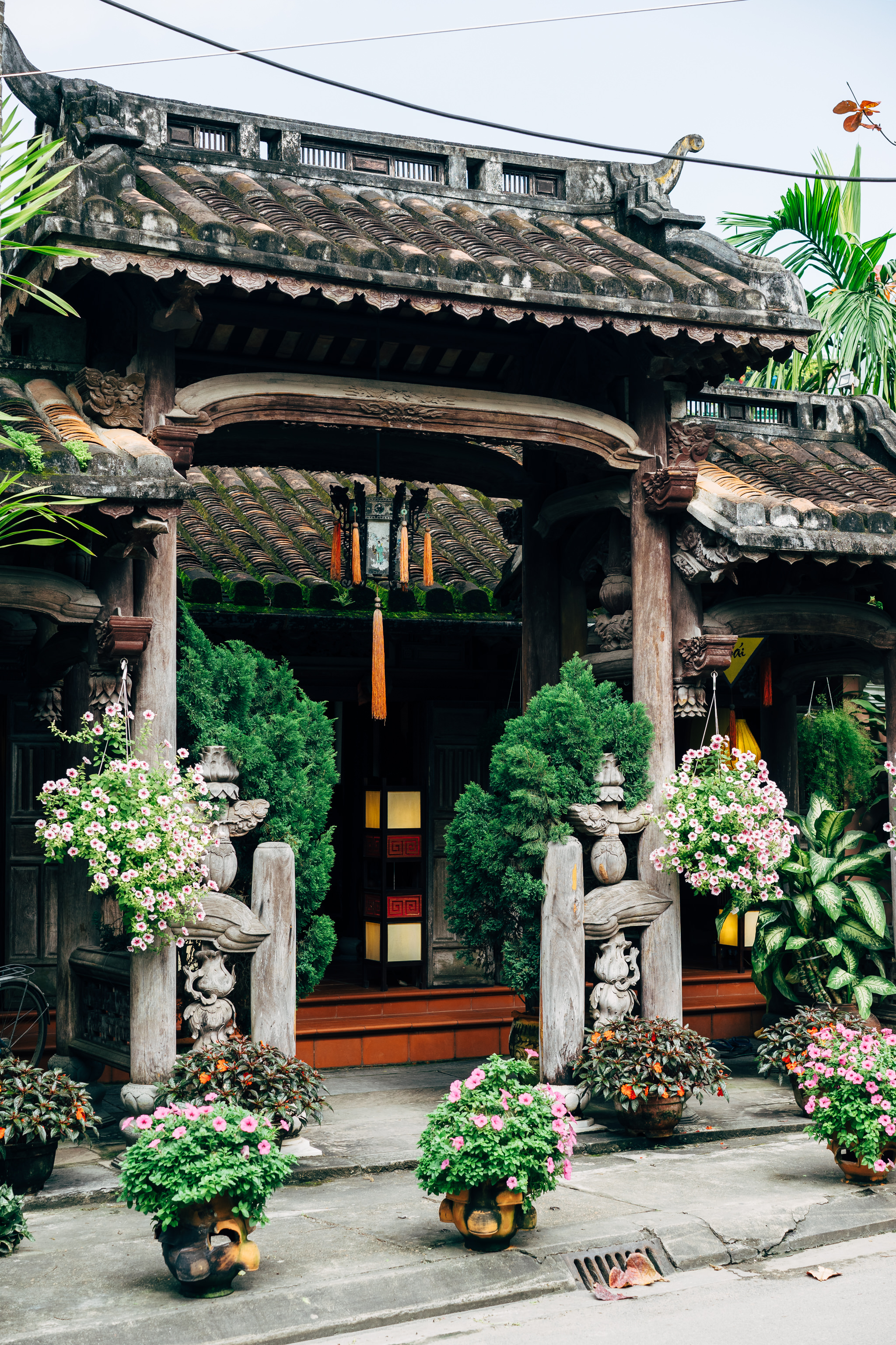 Ornate, moss-covered Hoi An building entrance with hanging flower baskets.