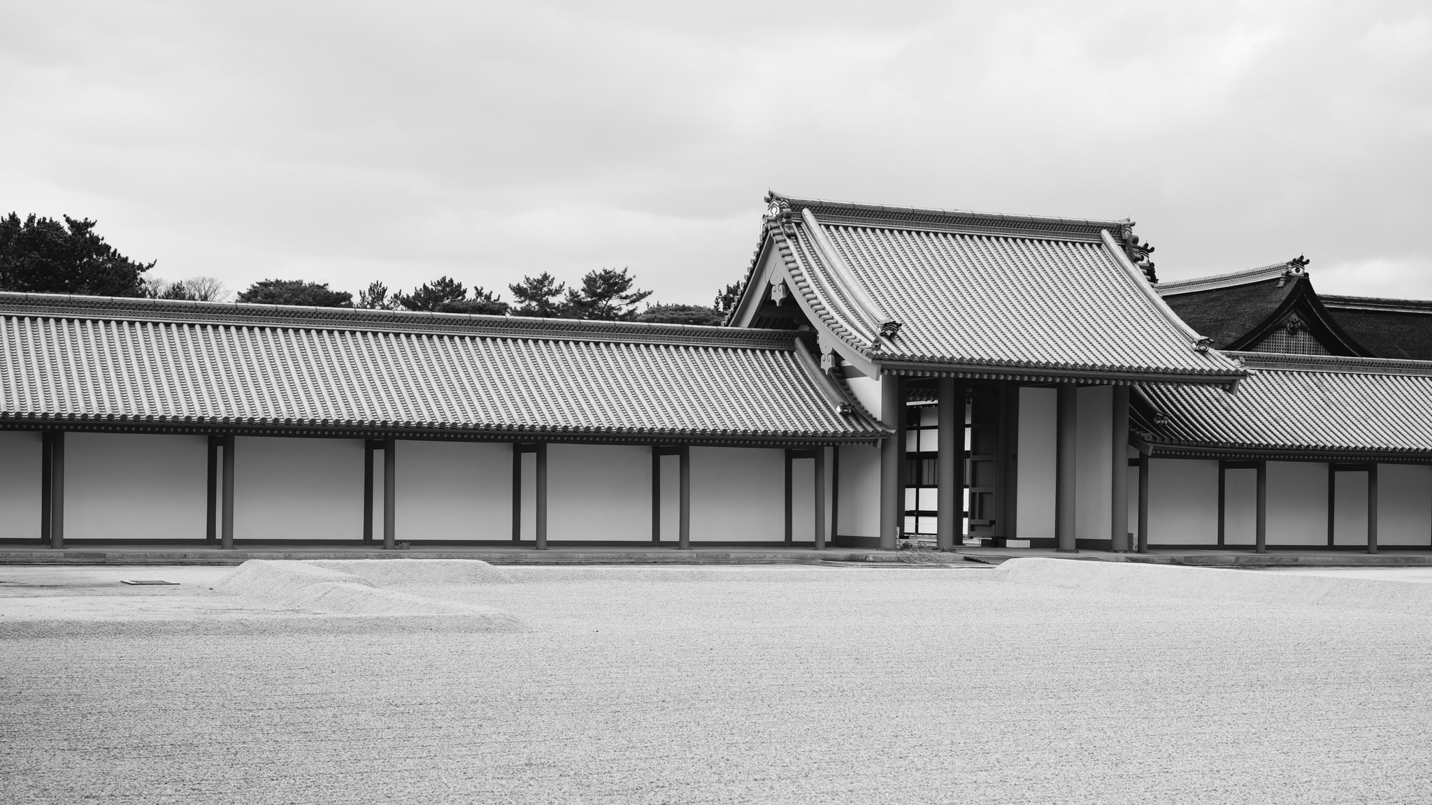 Black and white photo of Kyoto Gosho's exterior, featuring a long building with a tiled roof and white walls, set against a gravel courtyard.