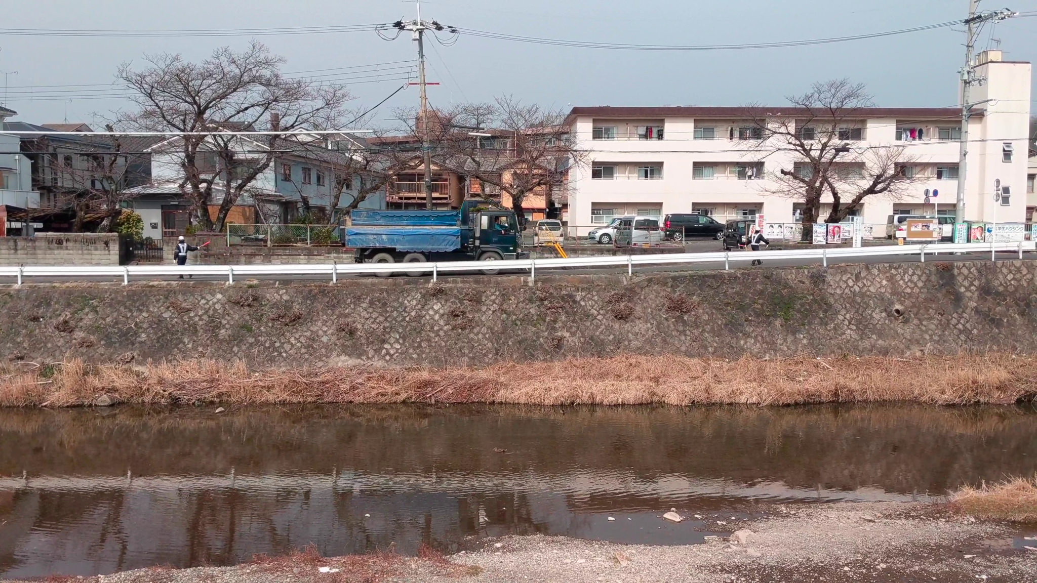 A blue truck parked on a road next to a river in Kyoto, Japan.