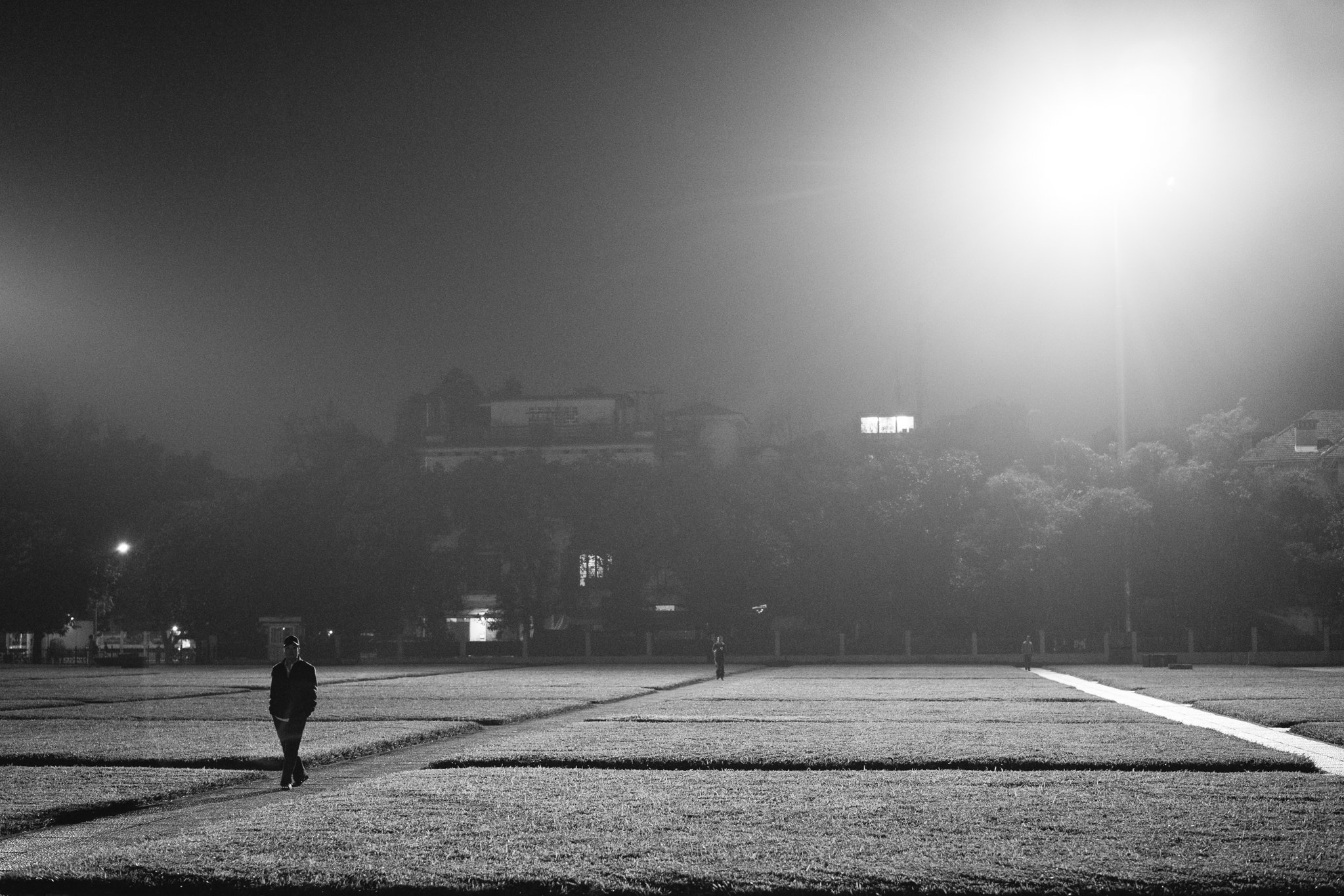Black and white photo of a person walking alone at night across a grassy field.