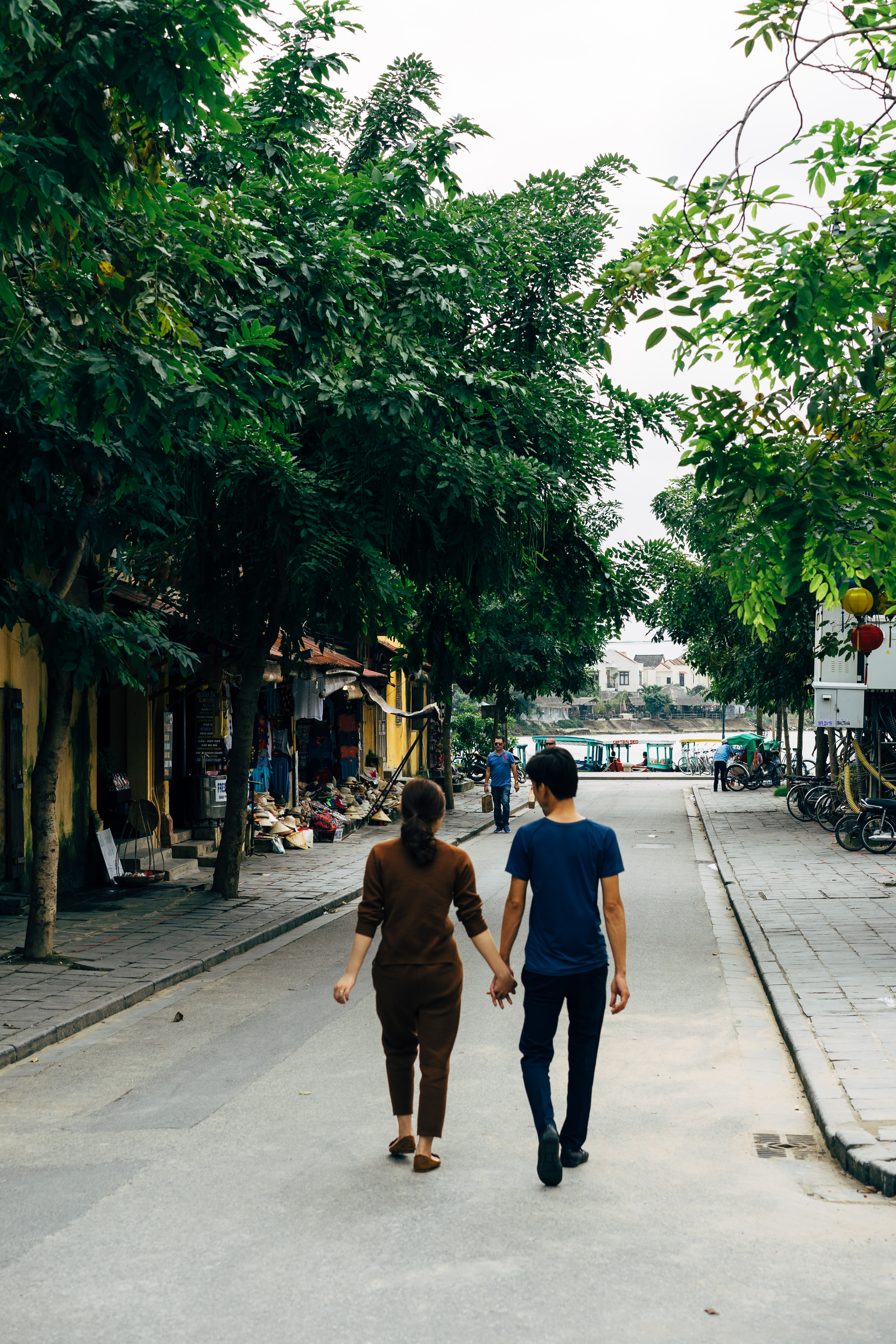 Couple holding hands walking down a street in Hoi An's old town.