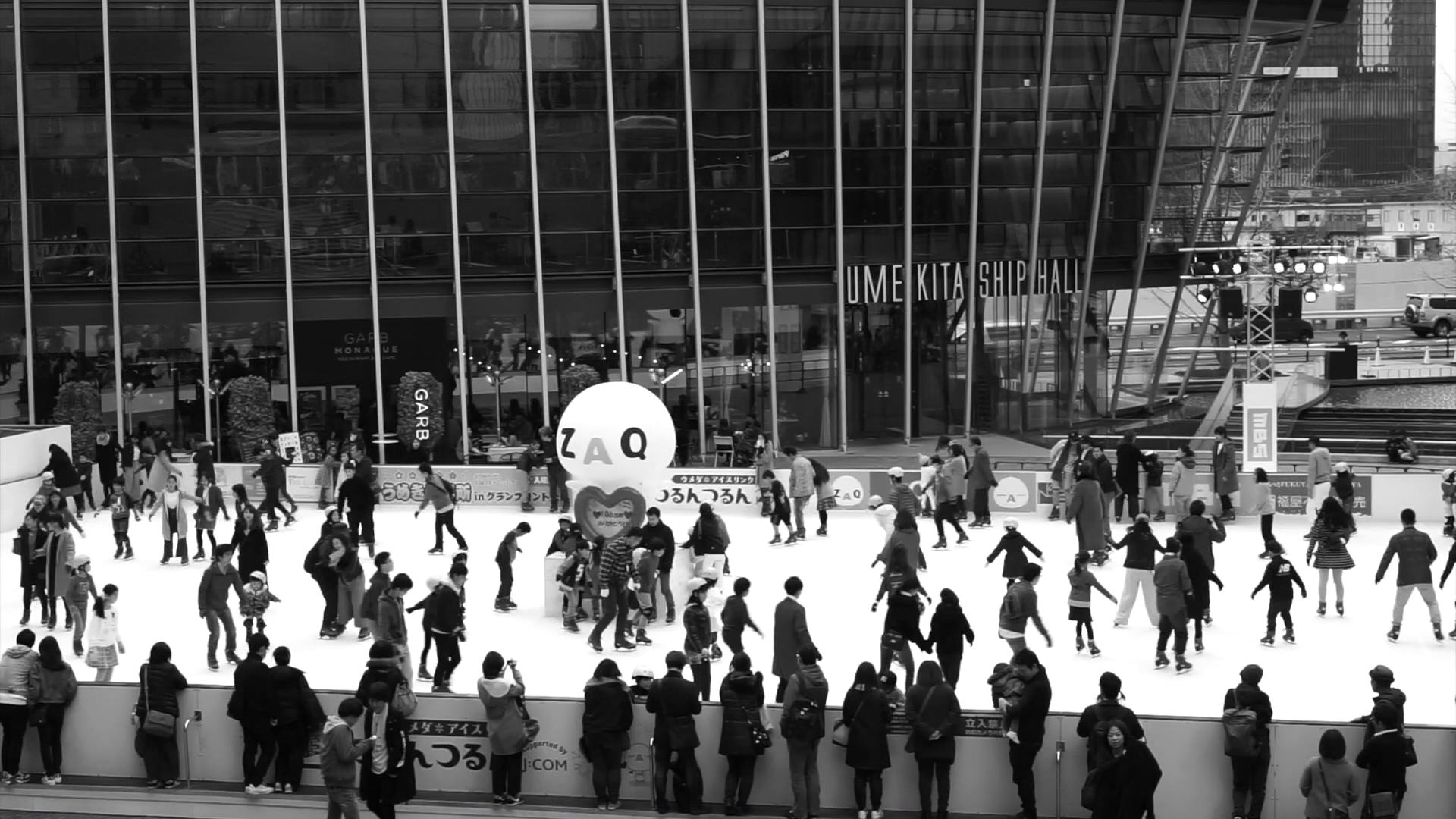 Black and white photo of an outdoor ice skating rink in Osaka, Japan, surrounded by people.