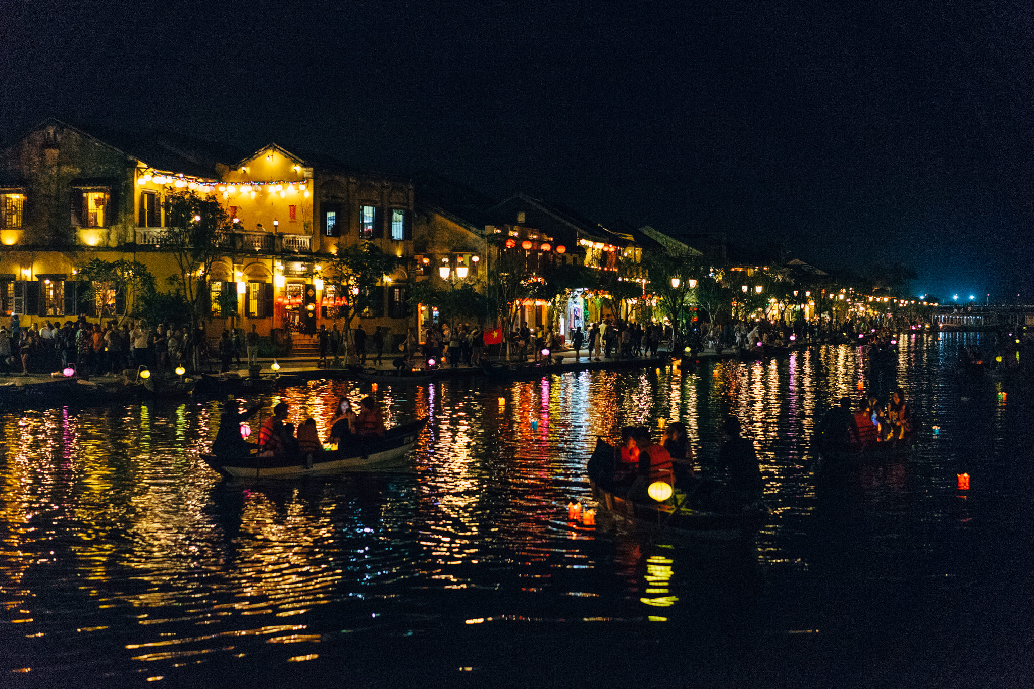 Hoi An river at night with illuminated buildings and people in boats.