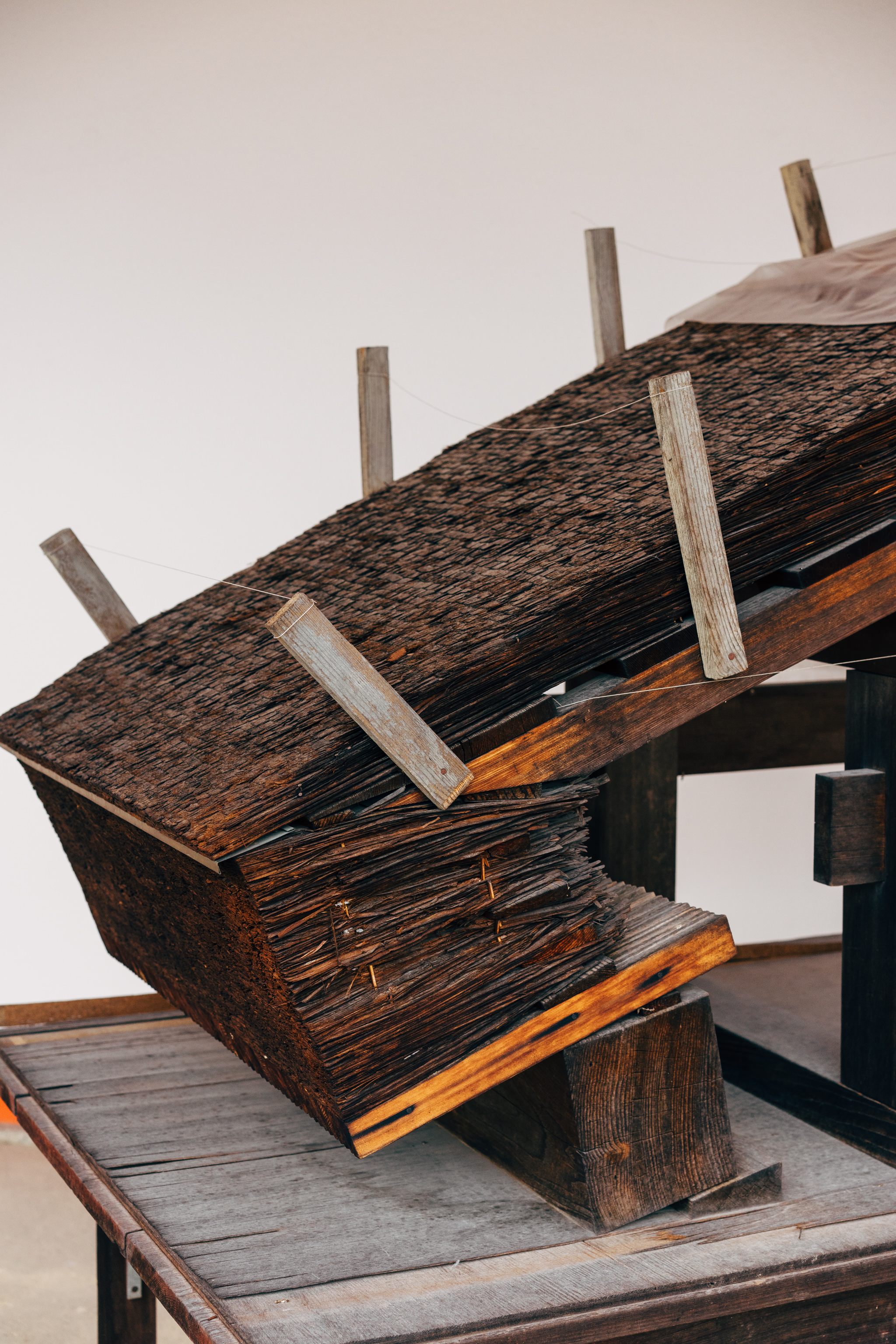 Close-up of a weathered wooden roof structure, possibly a model, showing its layered construction and wooden pegs.