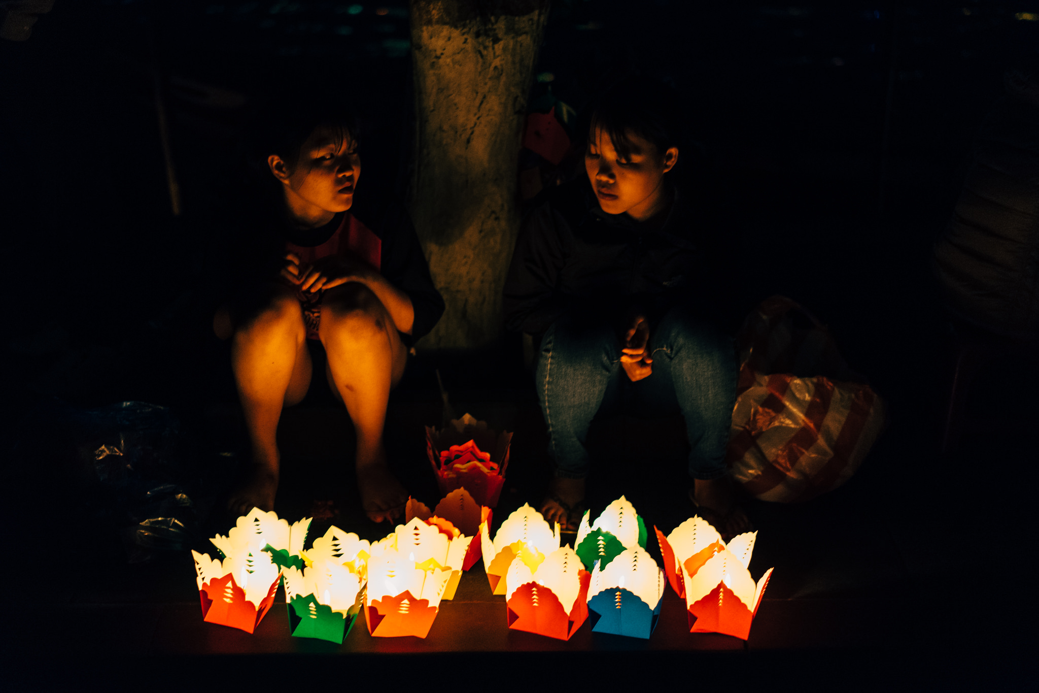Two young women sit in the dark next to several lit paper lanterns.
