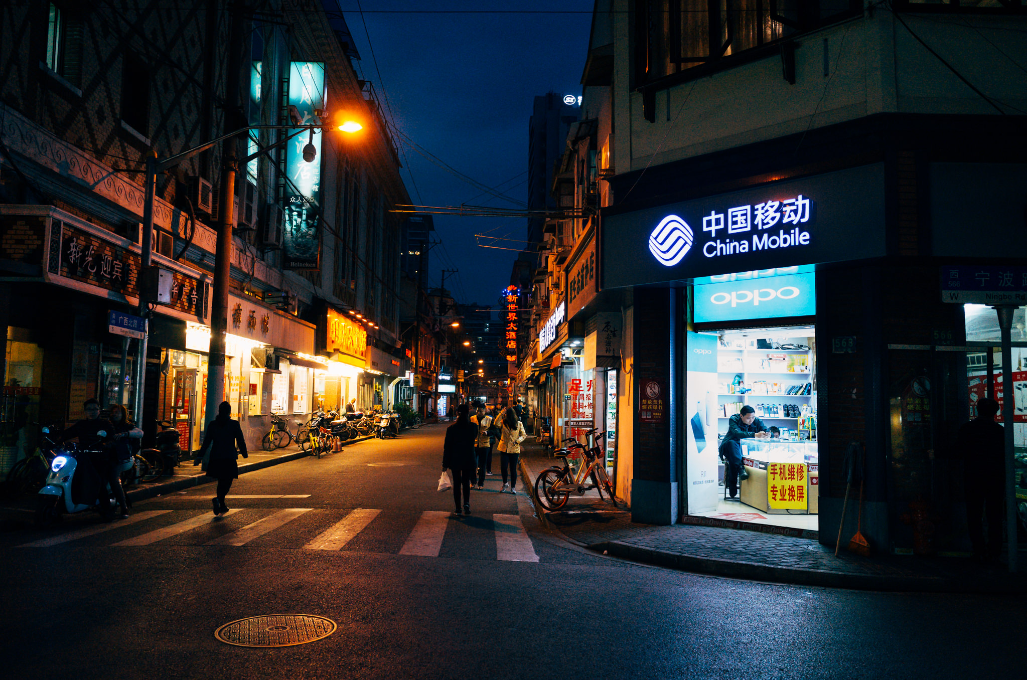 Night street scene in Shanghai, China, showing pedestrians and shops; a China Mobile store is prominent.