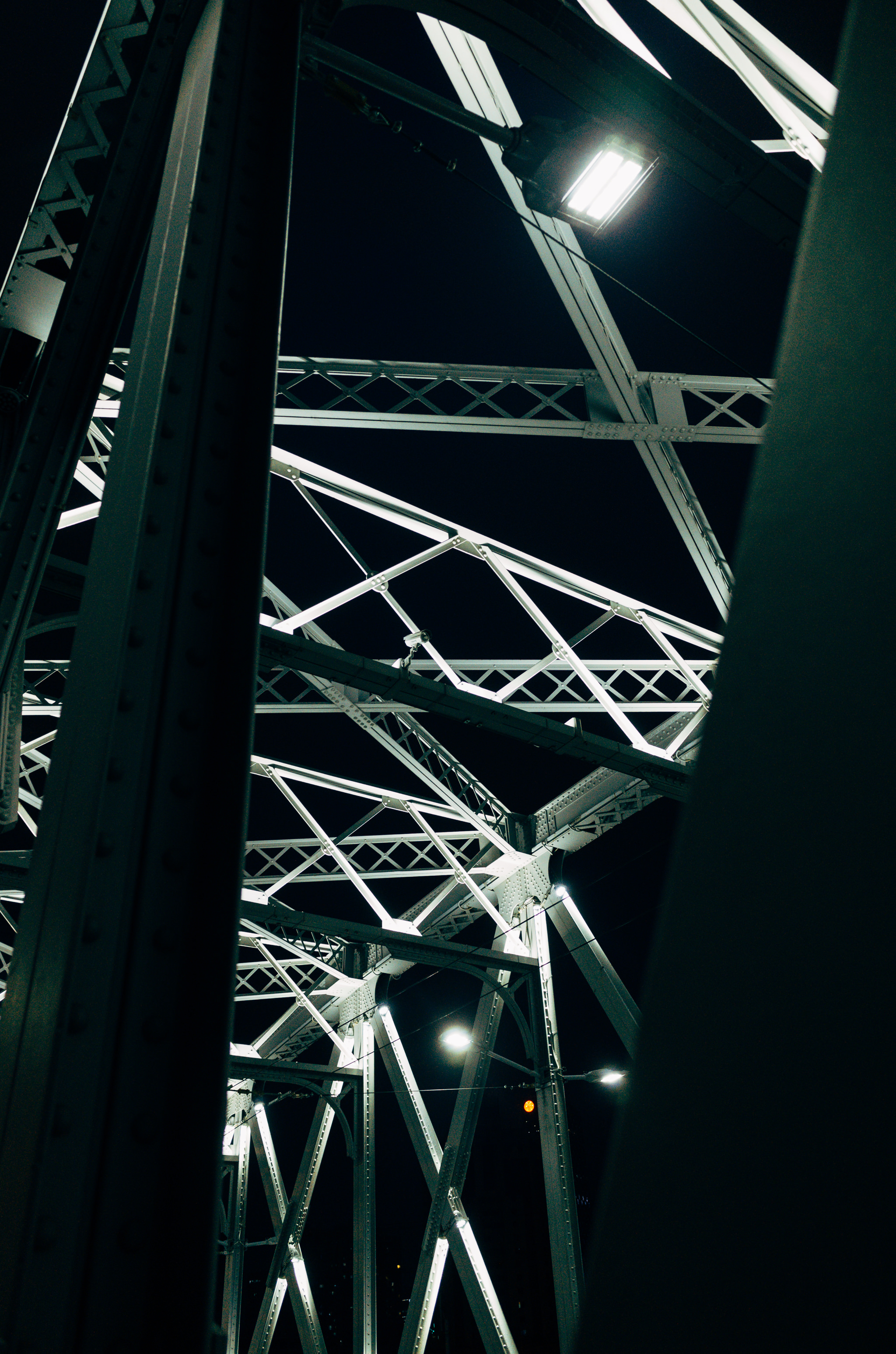 Low-angle close-up of a bridge's illuminated metal framework at night.