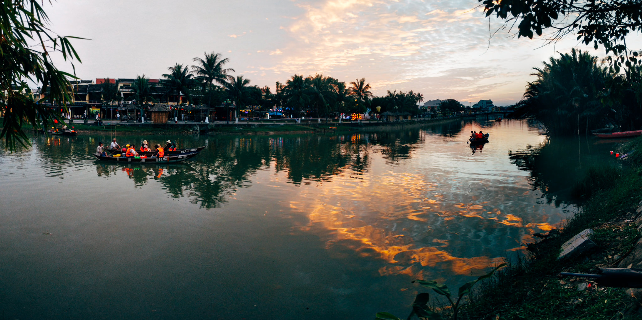 Sunset over Hoi An river in Vietnam, with boats carrying people.