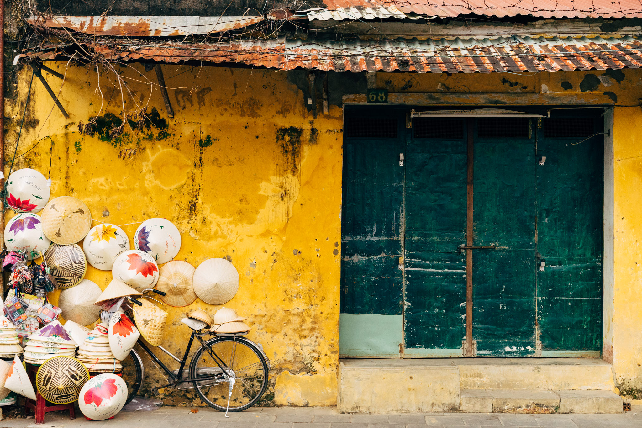 Vietnamese conical hats stacked near a bicycle leaning against a yellow building with a teal door.