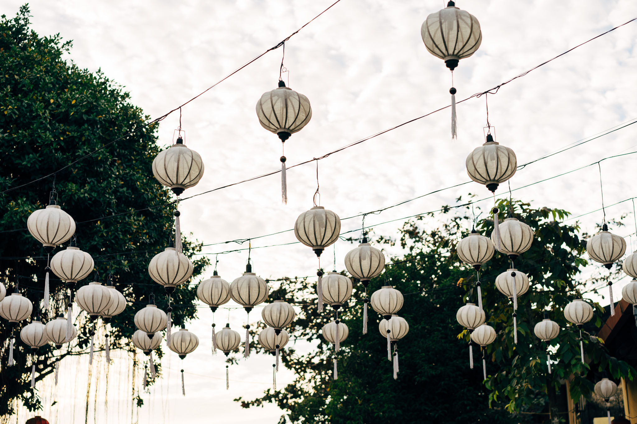 Many white Vietnamese lanterns hanging from wires against a cloudy sky.