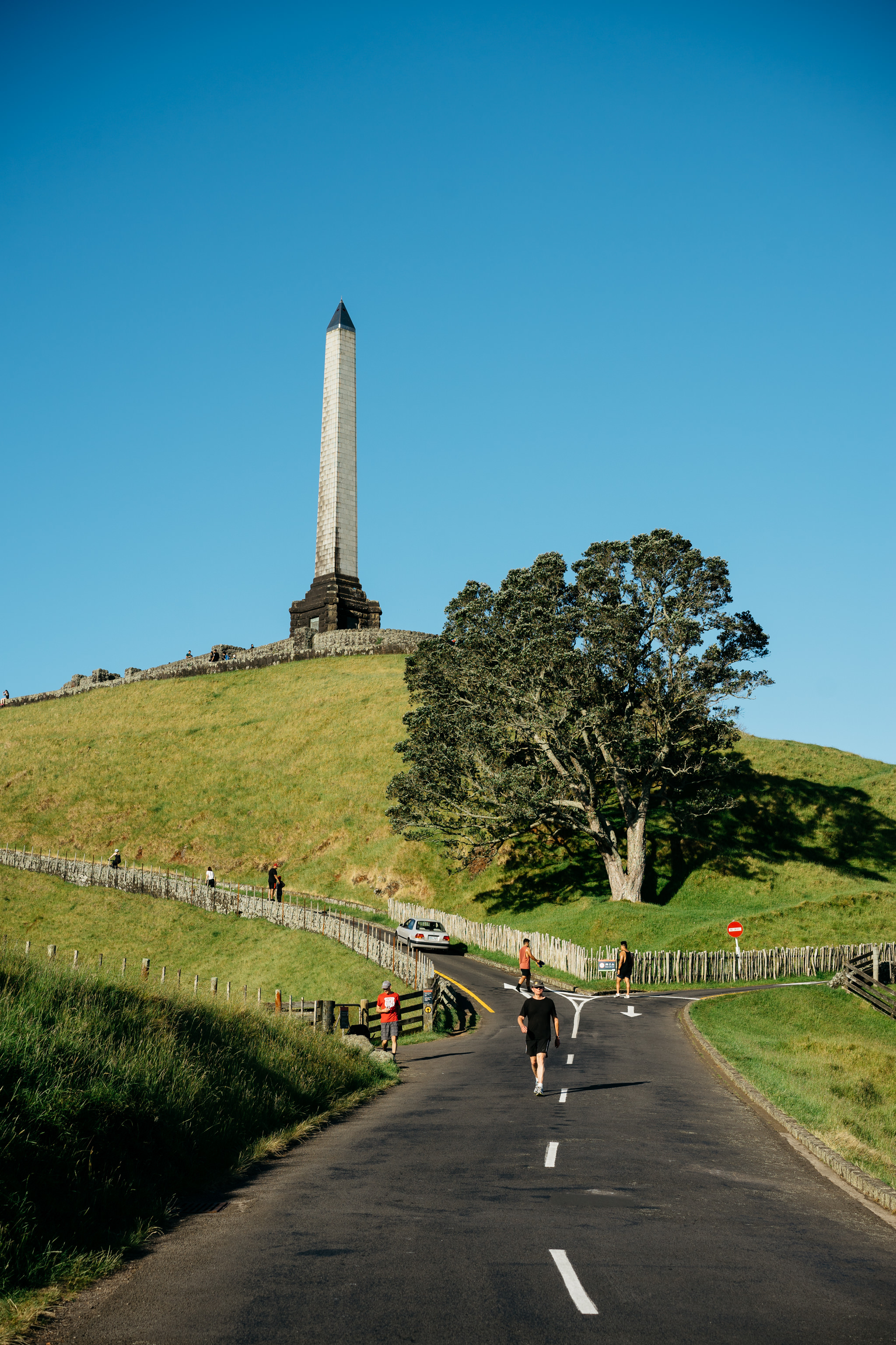 Man jogging on road toward obelisk on grassy hill.