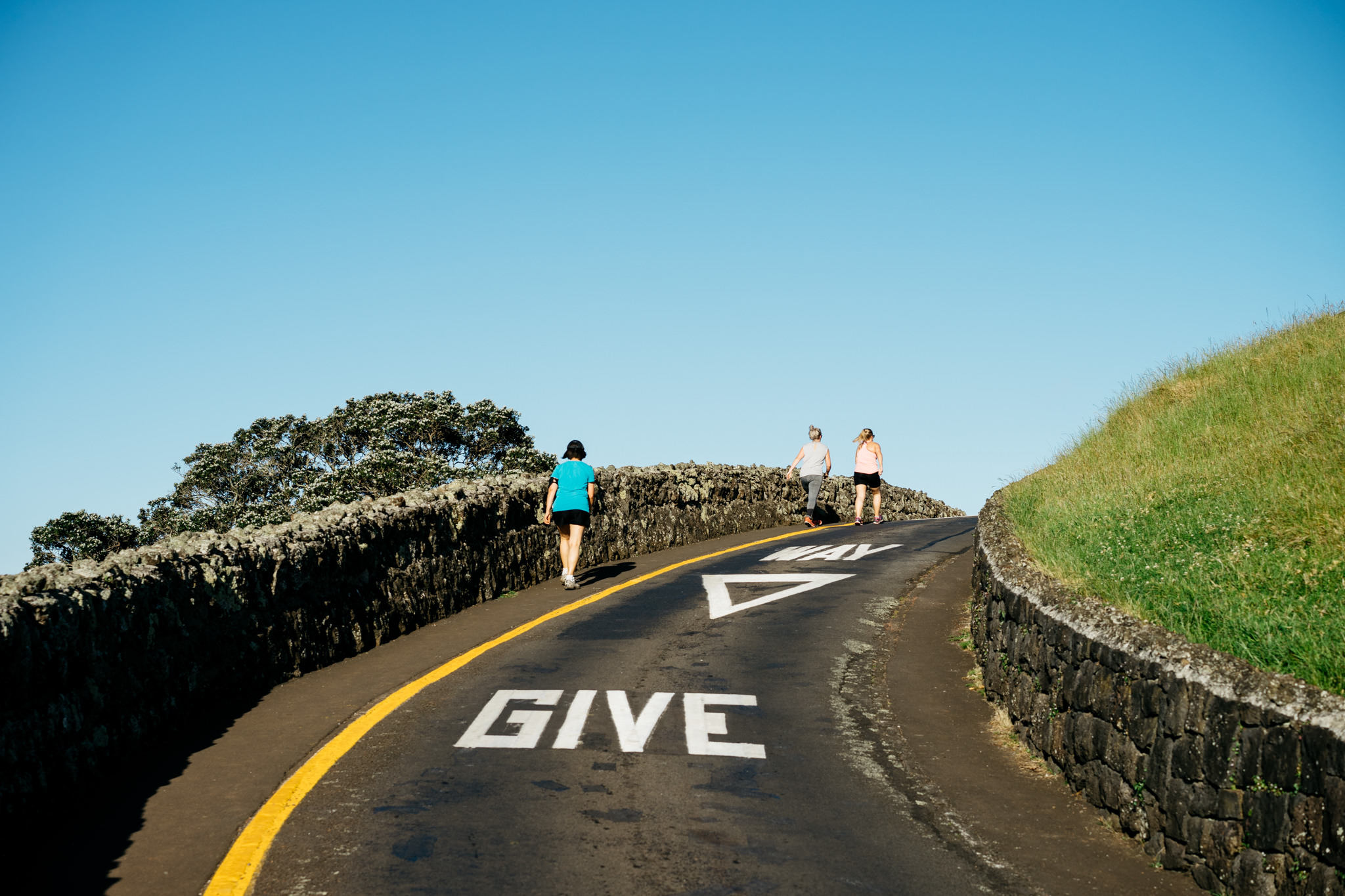 Three people walking away on a road with 'GIVE WAY' markings.