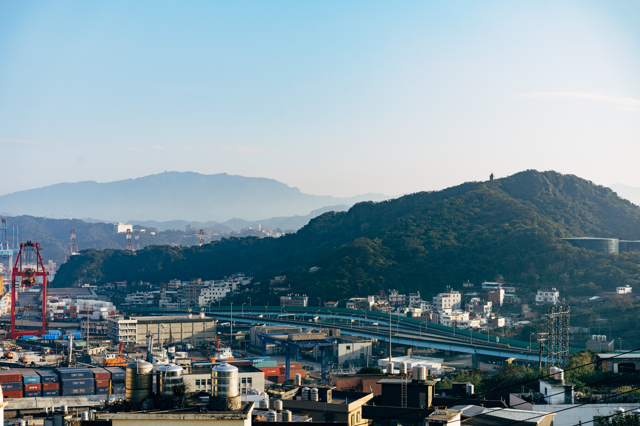 Keelung Harbor, Taiwan: a panoramic view of the port city nestled between mountains, featuring container stacks, cranes, and an elevated highway.